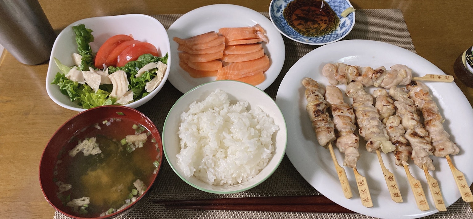 Spiedini di pollo grigliati, riso bianco, zuppa di miso, insalata, pomodori, carote su un piatto