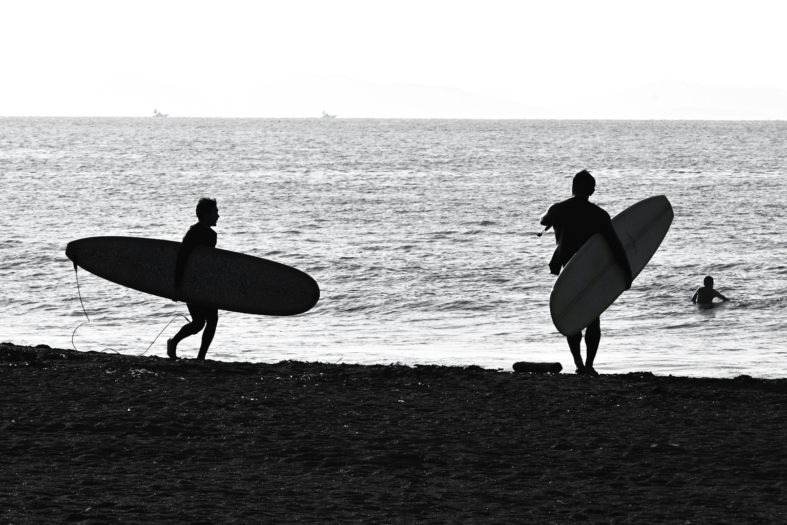 Silhouette de deux surfeurs portant des planches de surf marchant vers l'océan