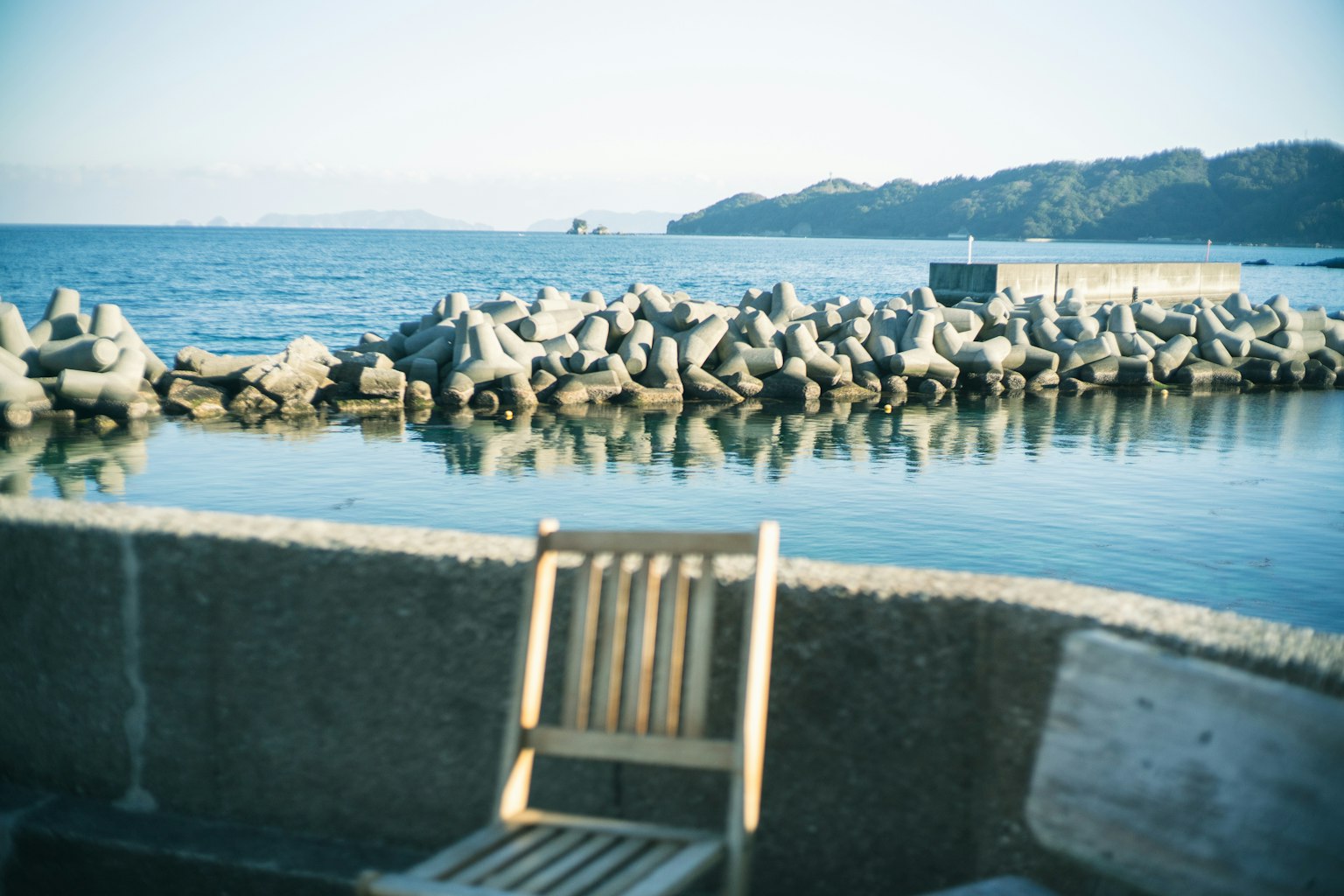 Une chaise en bois surplombant la mer avec un brise-lames en arrière-plan