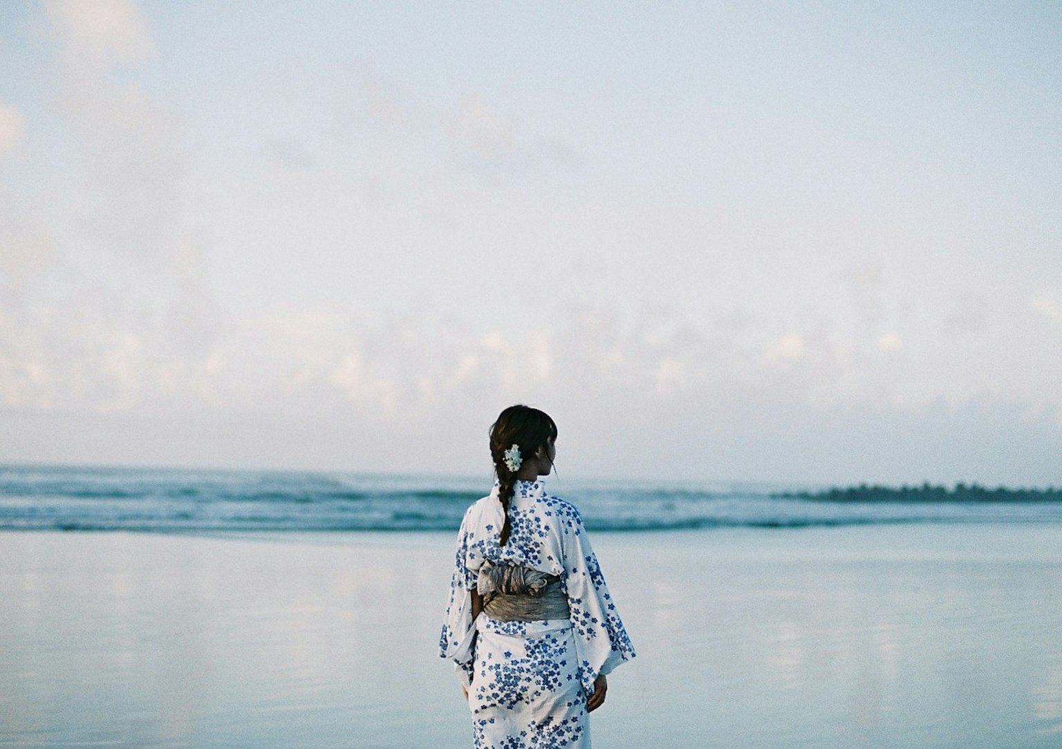 Femme en robe blanche se tenant sur la plage regardant vers l'océan