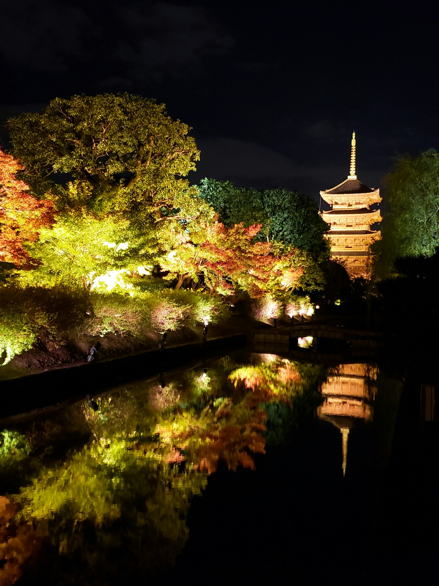 ทิวทัศน์ที่สวยงามของเจดีย์ที่สว่างในยามค่ำคืนสะท้อนอยู่ในบ่อน้ำที่มีใบไม้เปลี่ยนสี