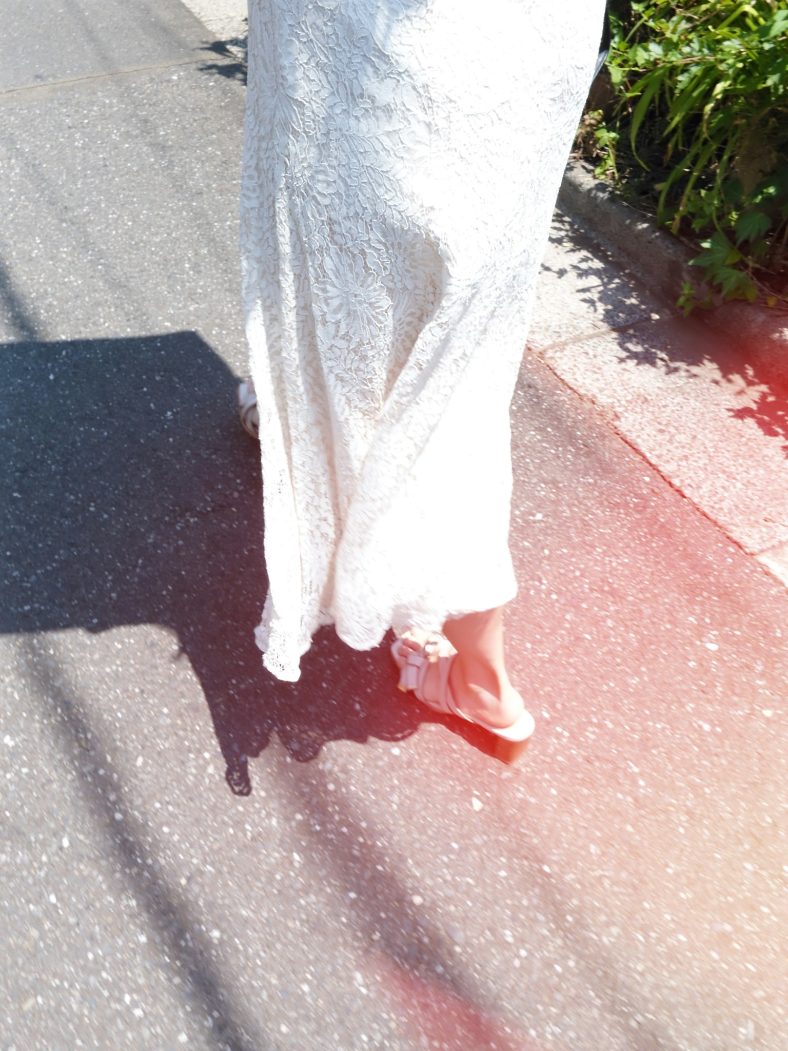 穿著白色裙子的女人在路上走，背景有綠色植物