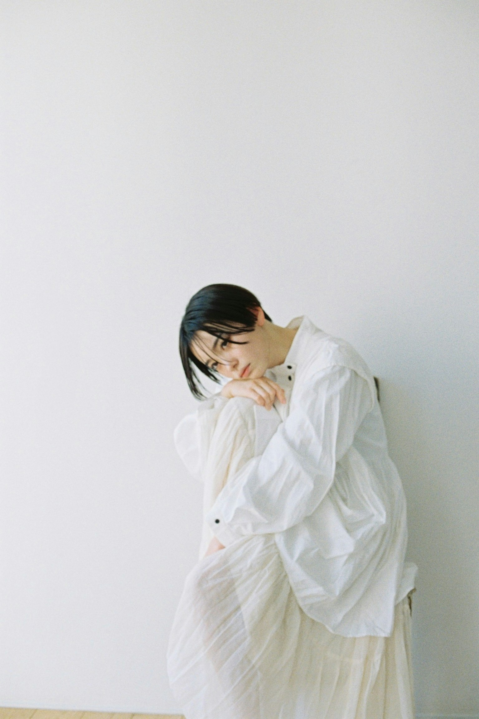 A woman in a white shirt leaning against a white wall