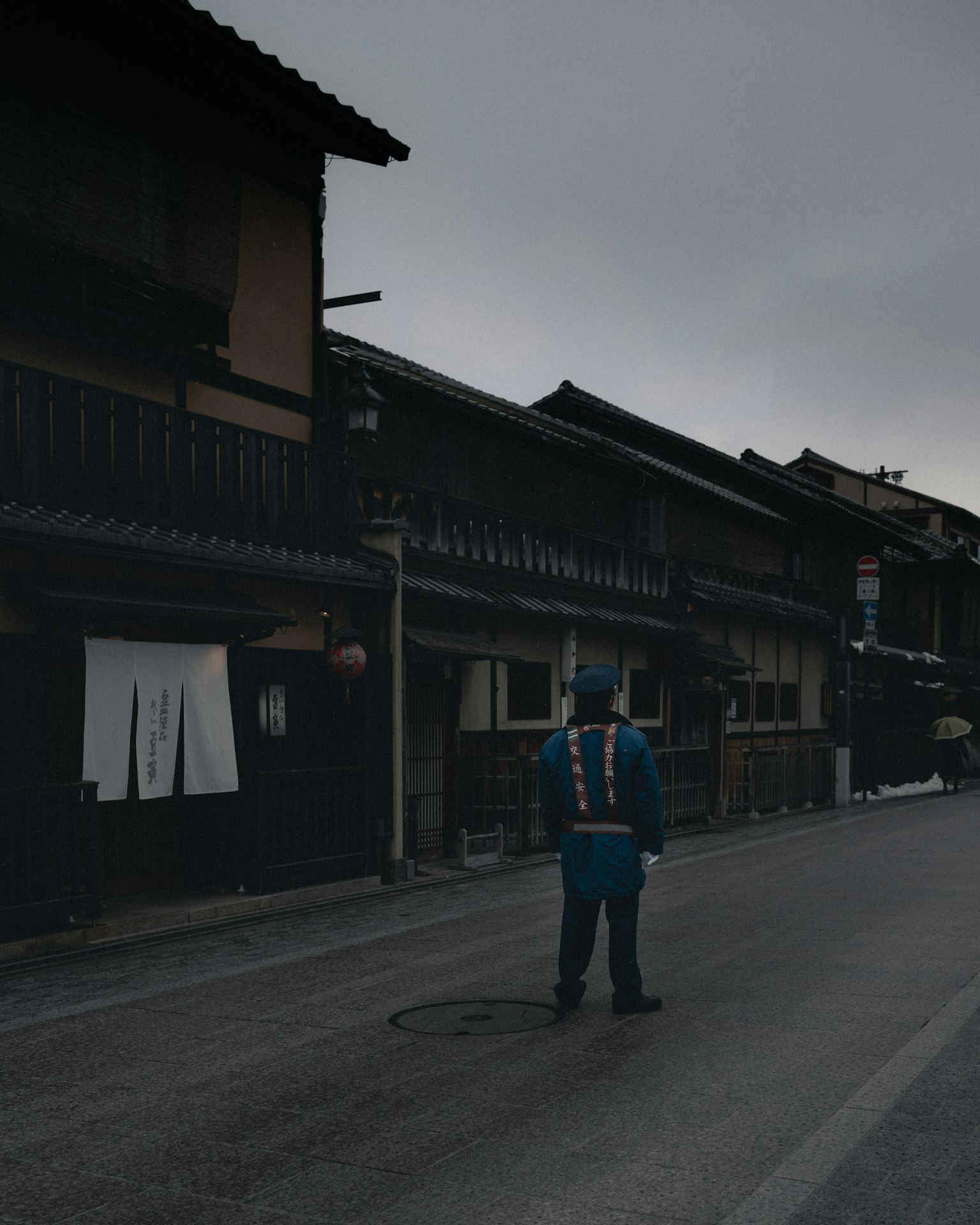 一个穿着蓝色制服的人站在一条安静的街道上，街道两旁是传统建筑