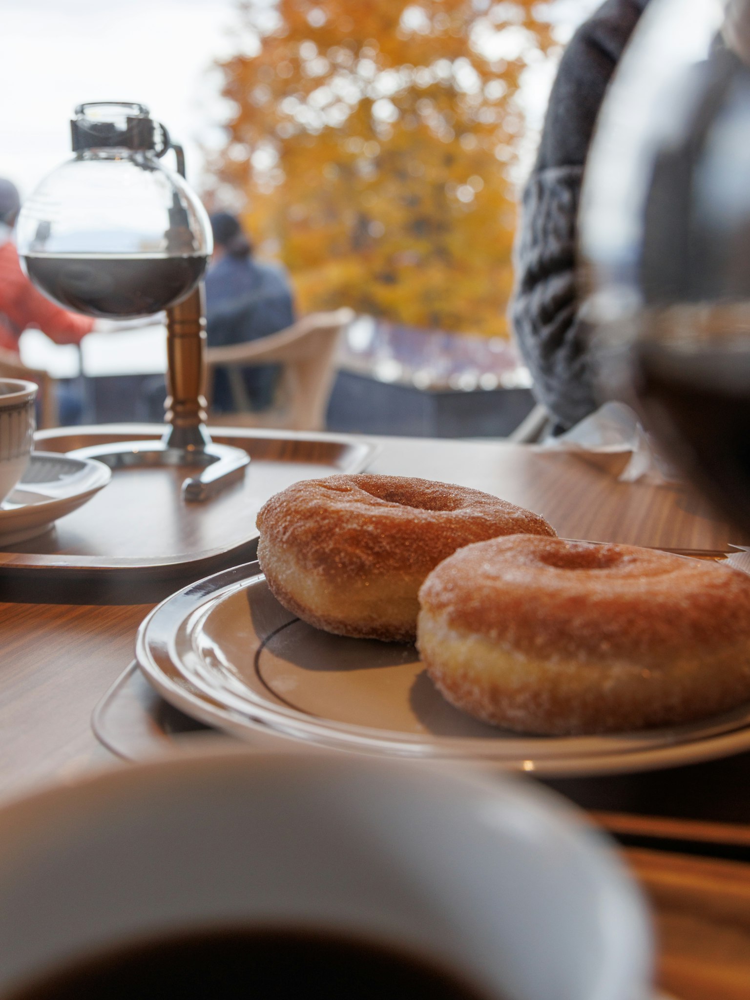 コーヒーとドーナツがテーブルに並び、背景には秋の木々が見える