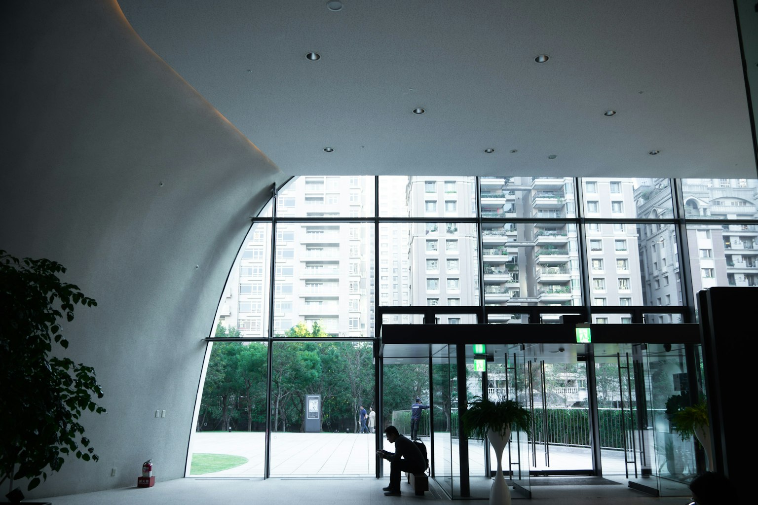 Interior view of a modern building entrance featuring large glass windows showing high-rise buildings and greenery