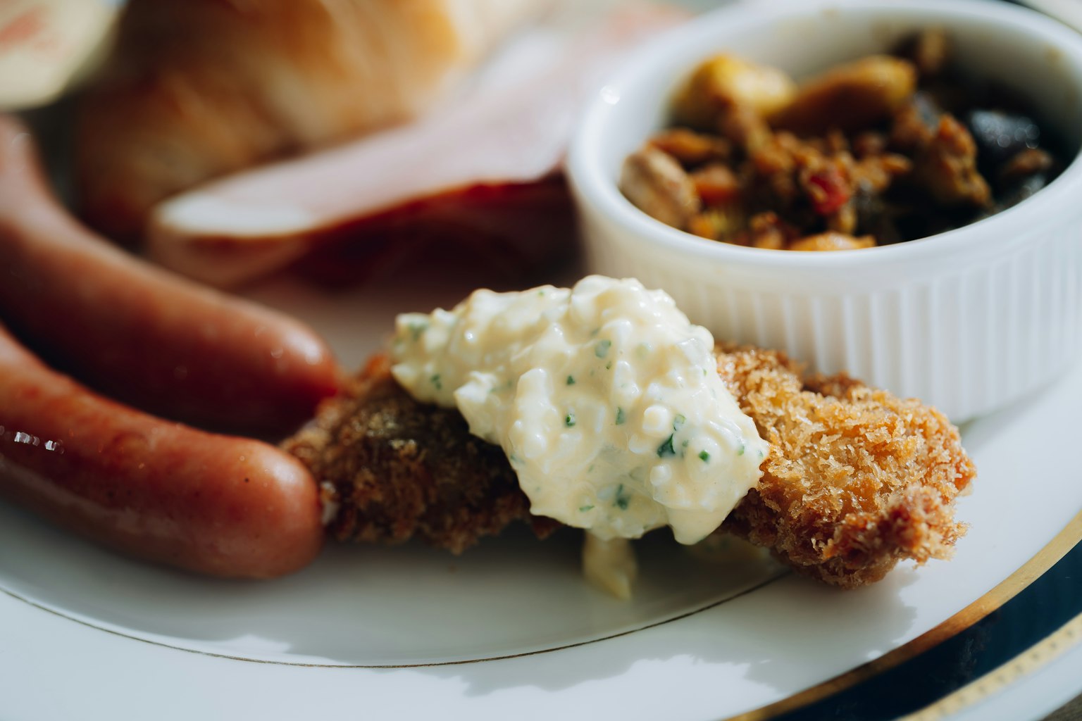 Plate of fried chicken with creamy sauce alongside sausages and slices of salami