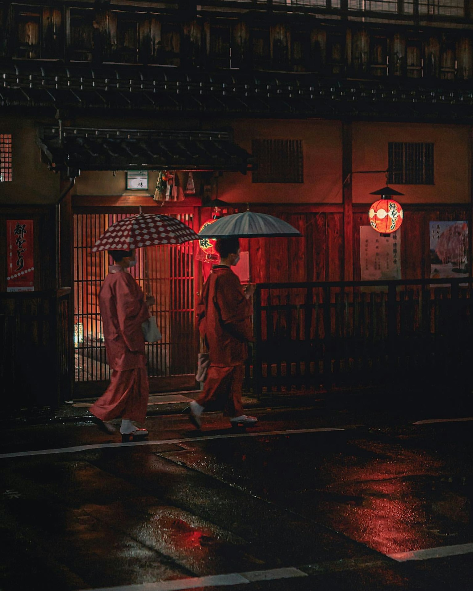 ผู้หญิงสองคนในชุดกิโมโนสีแดงเดินถือร่มในฉากถนนที่มีฝนตก