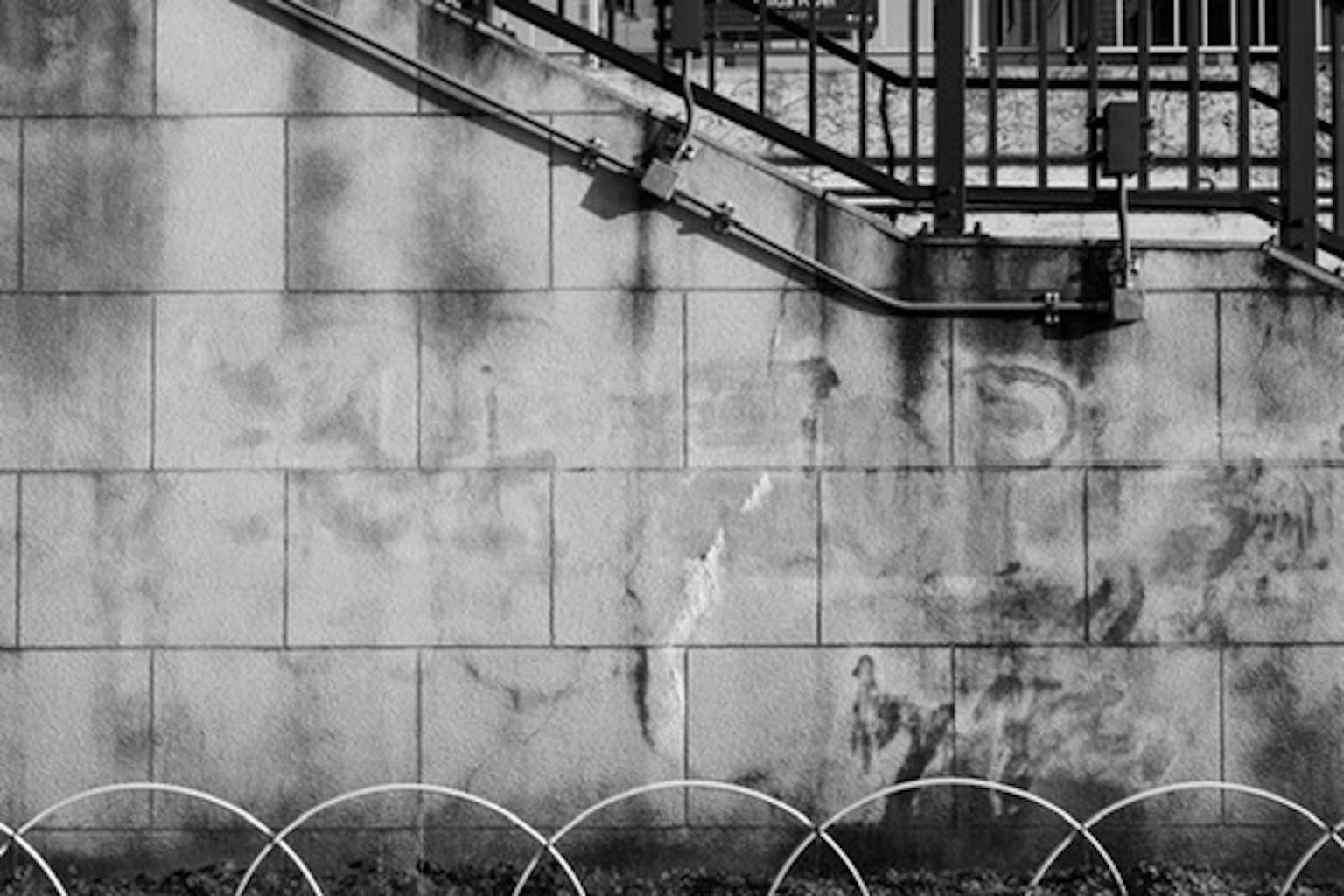 Black and white photo of a wall near stairs featuring worn tiles and a metal railing