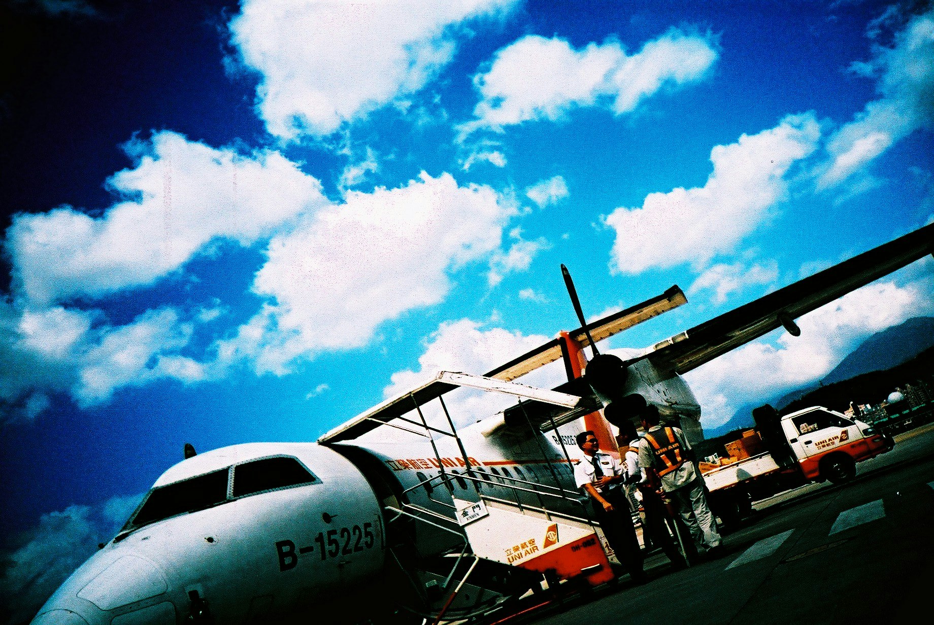 青空の下で並ぶ飛行機と整備スタッフのいる滑走路