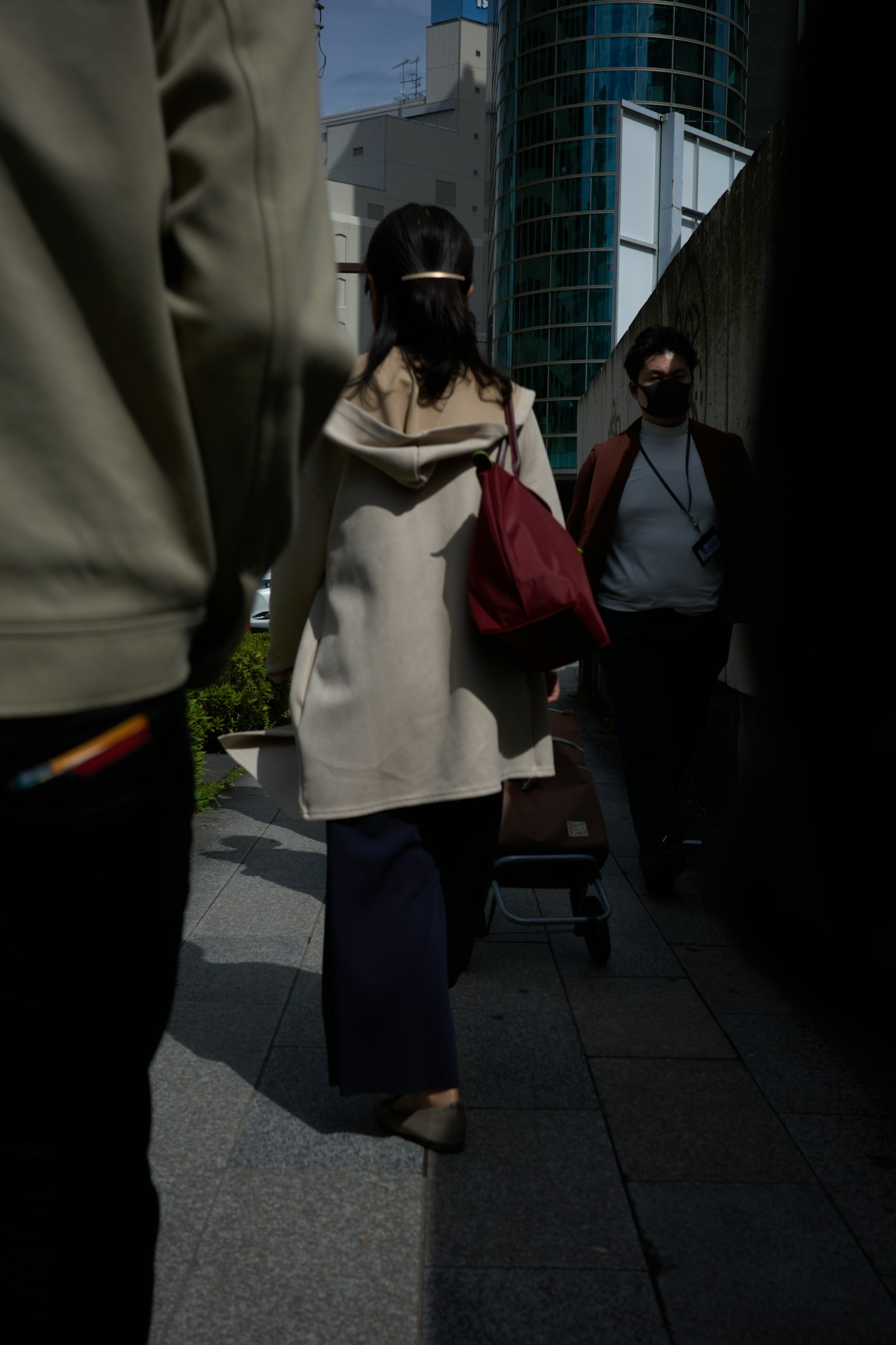 ผู้หญิงใส่เสื้อโค้ตสีเบจถือกระเป๋าสีแดงเดินในสภาพแวดล้อมเมือง