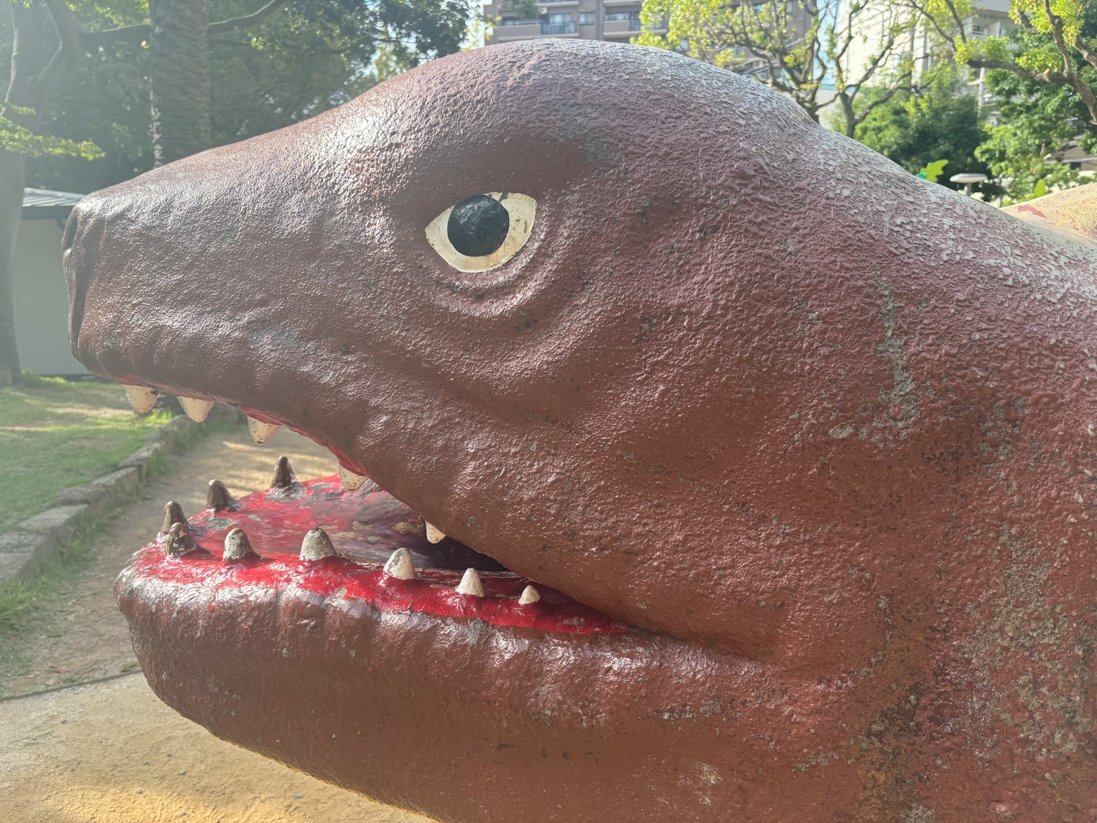 공원에 있는 공룡 머리의 클로즈업 생생한 빨간 입과 날카로운 이빨이 특징