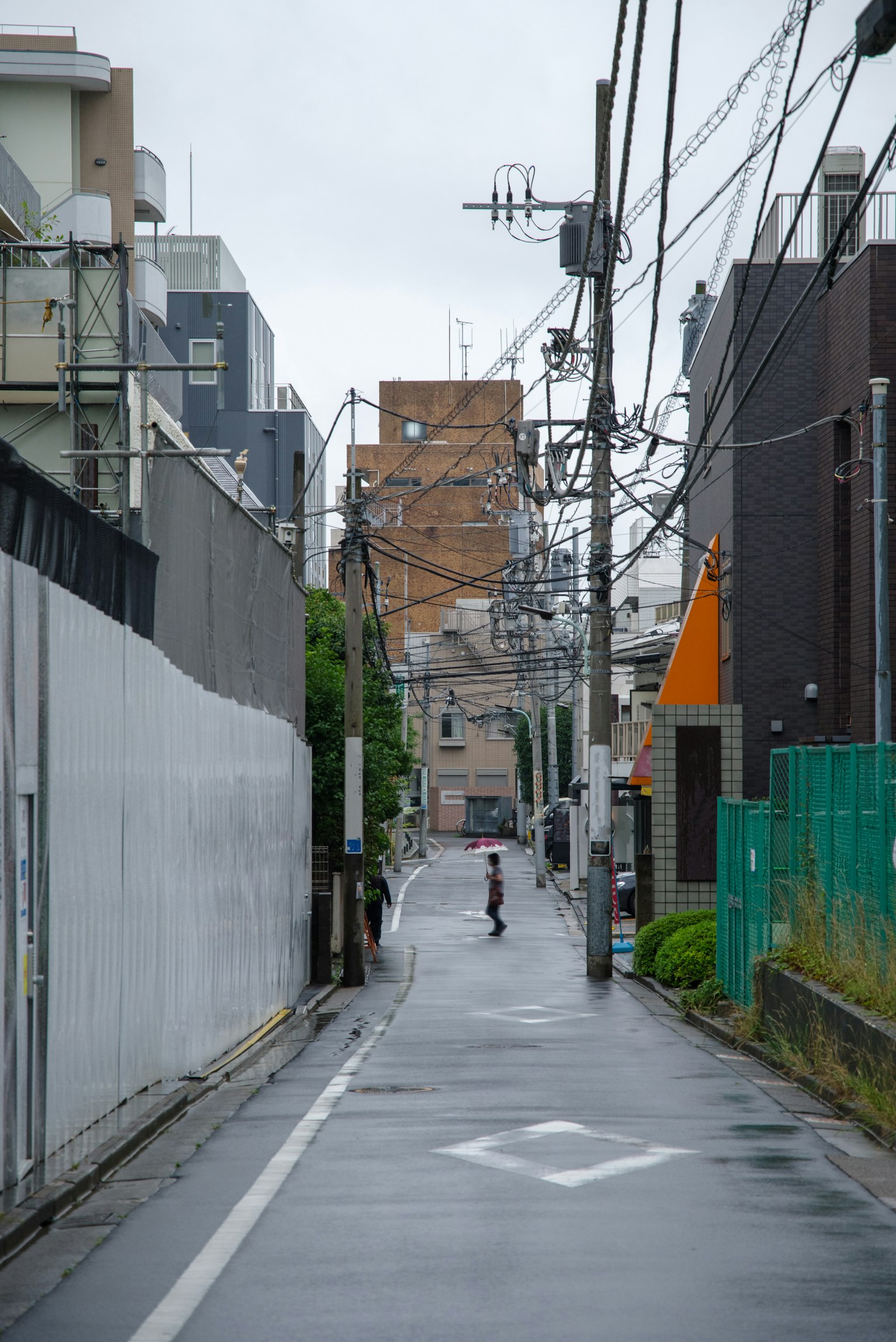 Schmale Gasse mit einer Person im Regen und Hochhäusern im Hintergrund