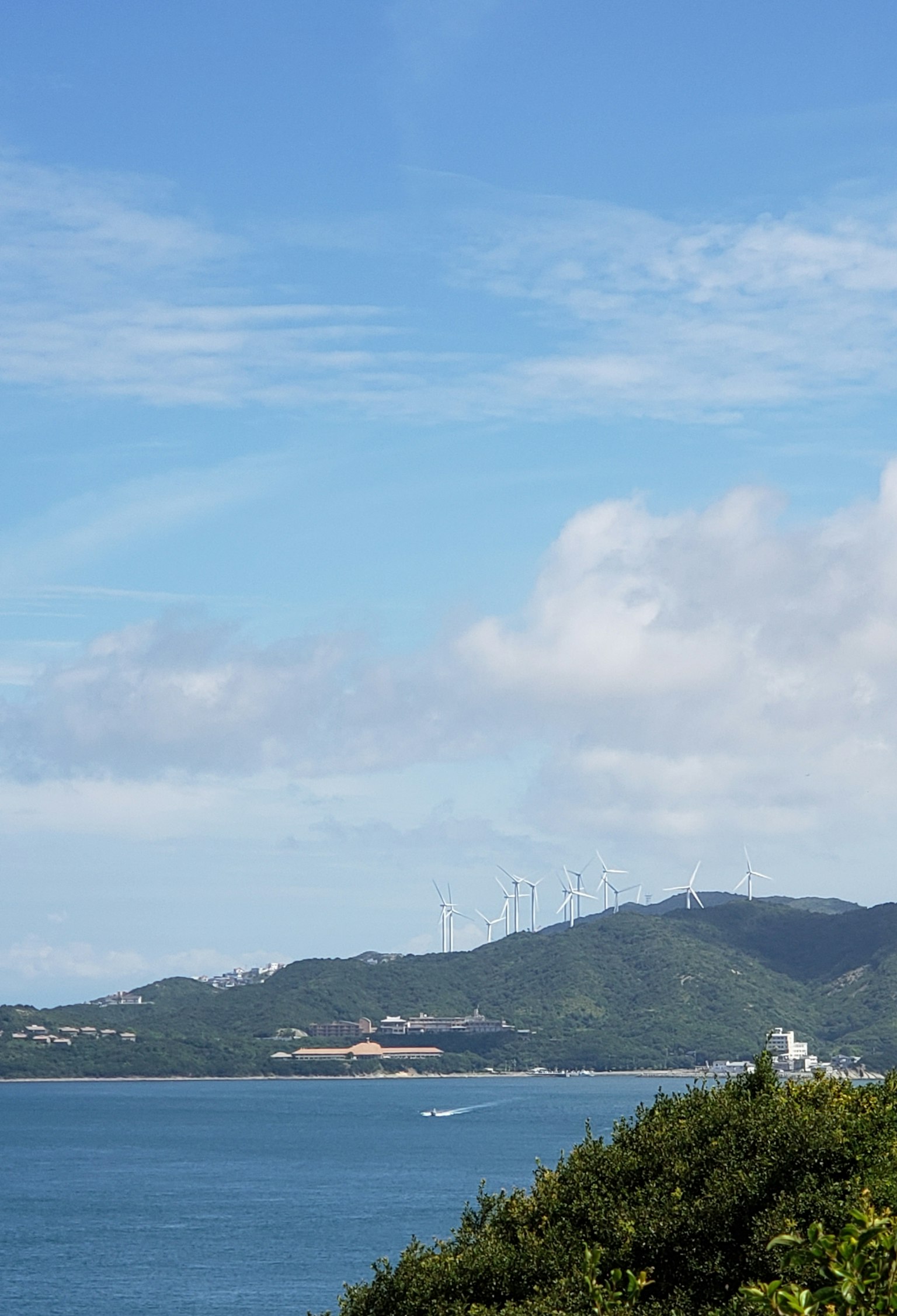 Paysage côtier sous un ciel bleu avec des nuages montrant des collines et un bateau