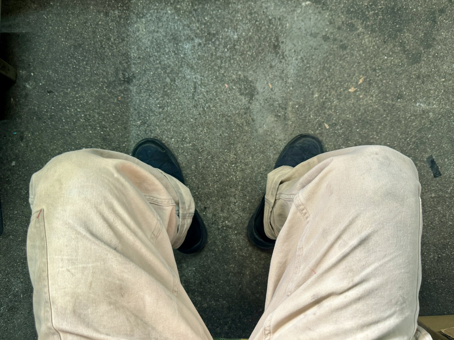 Foto delle gambe di una persona seduta per terra con pantaloni chiari e scarpe nere