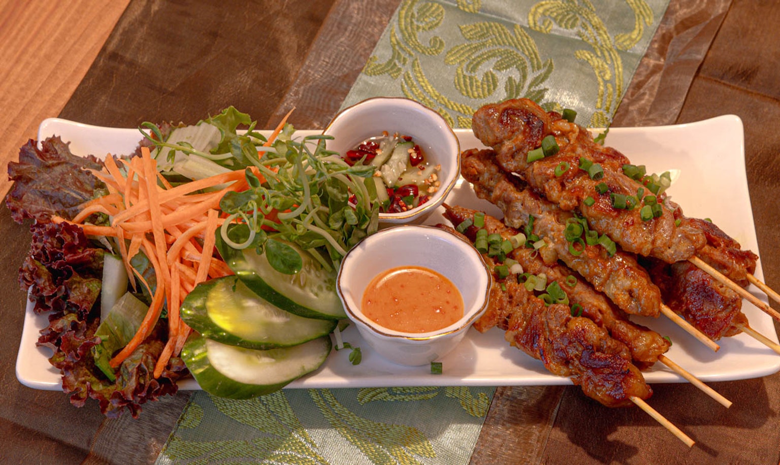 Tusuk sate panggang dengan salad segar yang menampilkan sate ayam dan saus