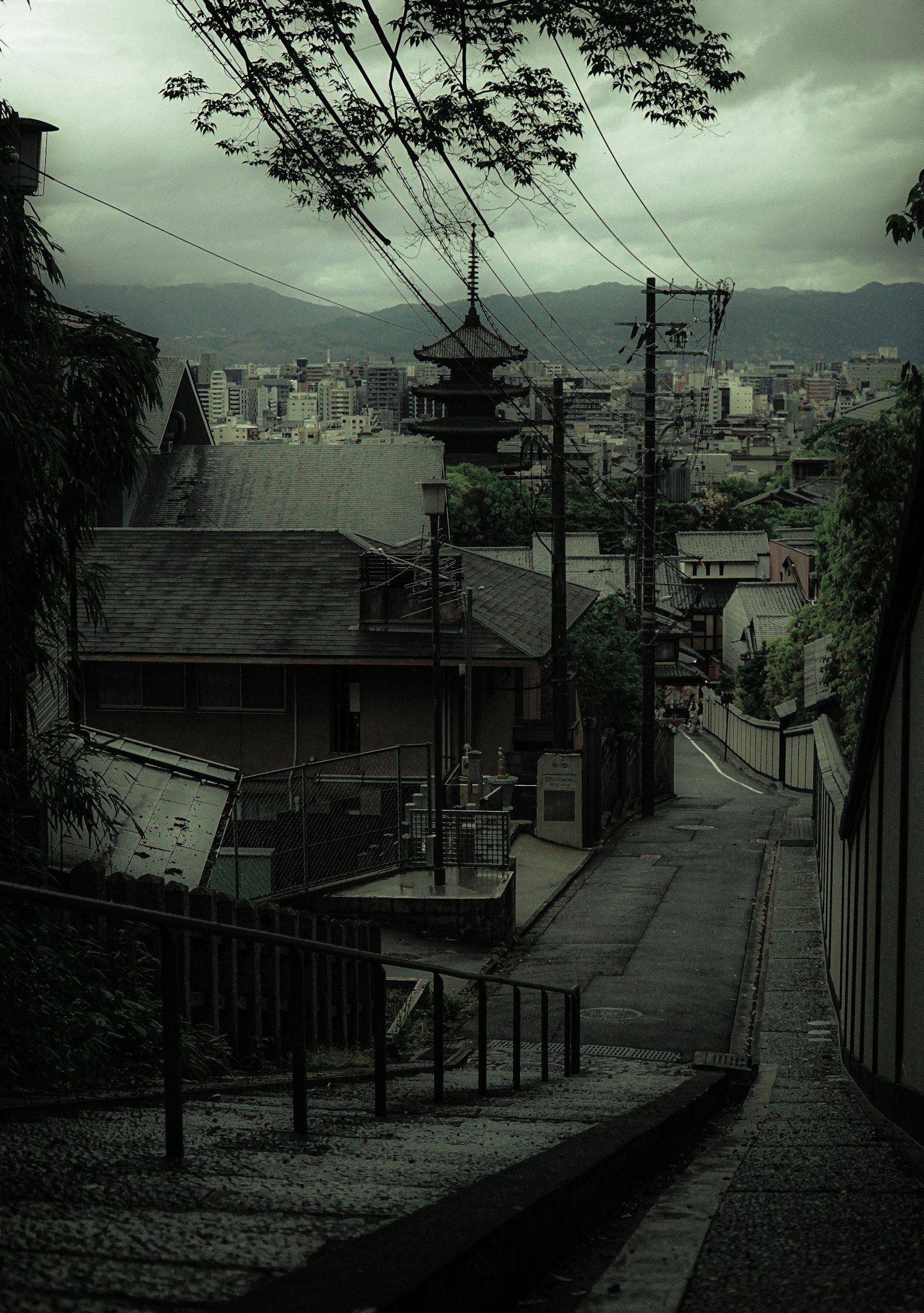 A dark, cloudy cityscape with a narrow slope featuring old buildings and utility poles