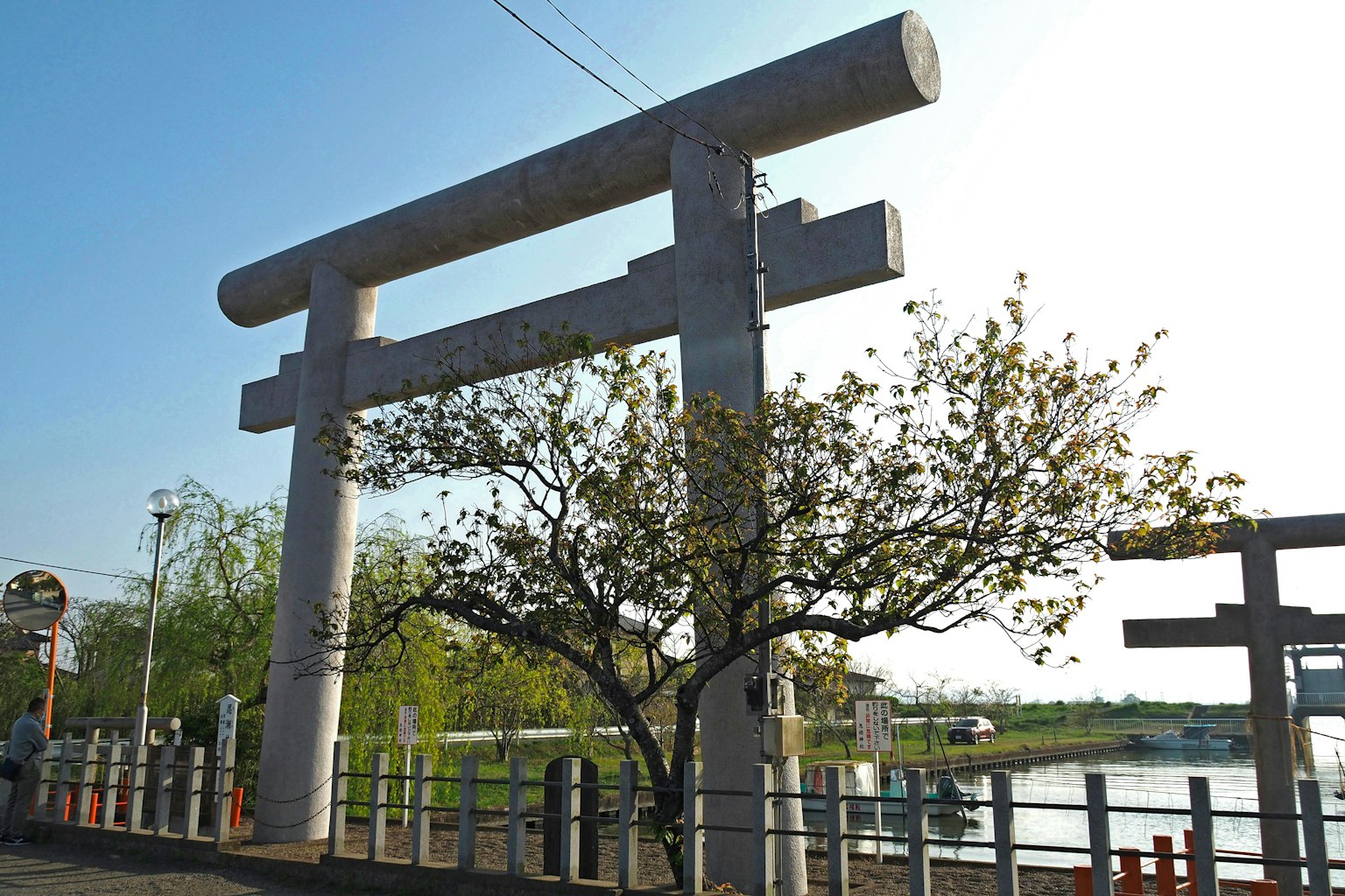 Grande porta torii in cemento con alberi verdi e un fiume vicino