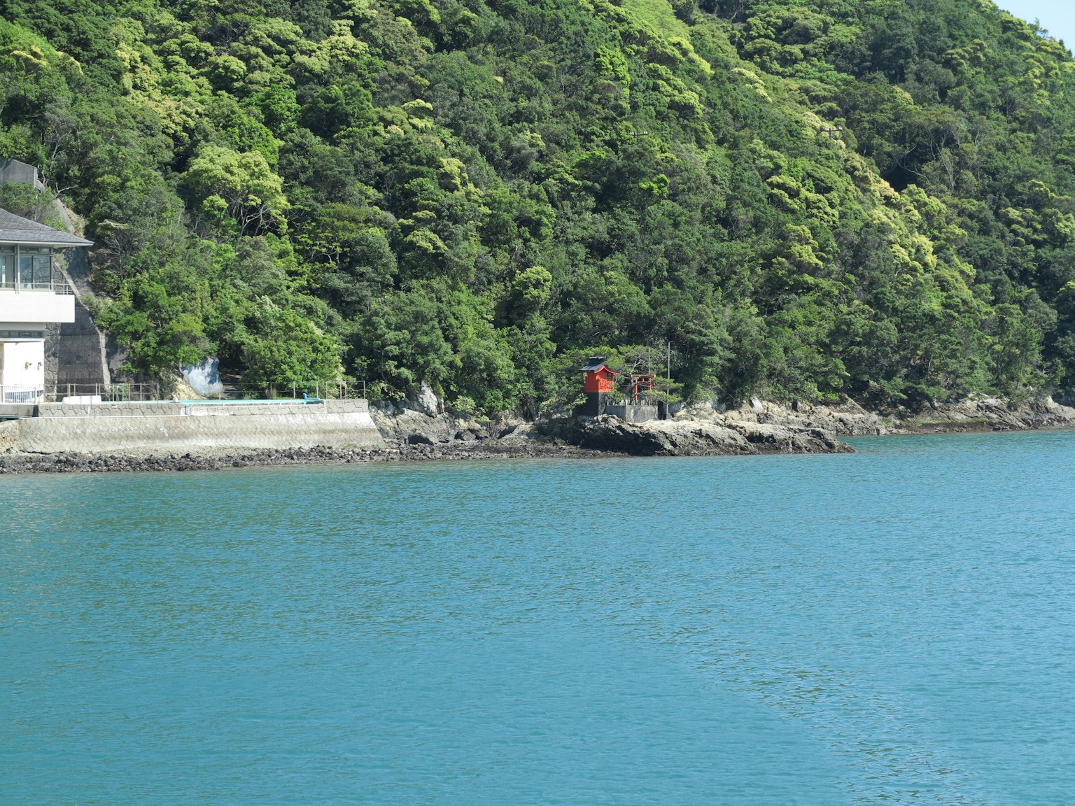 Scenic coastline with blue water and lush green hills a person in a red outfit stands near the rocks