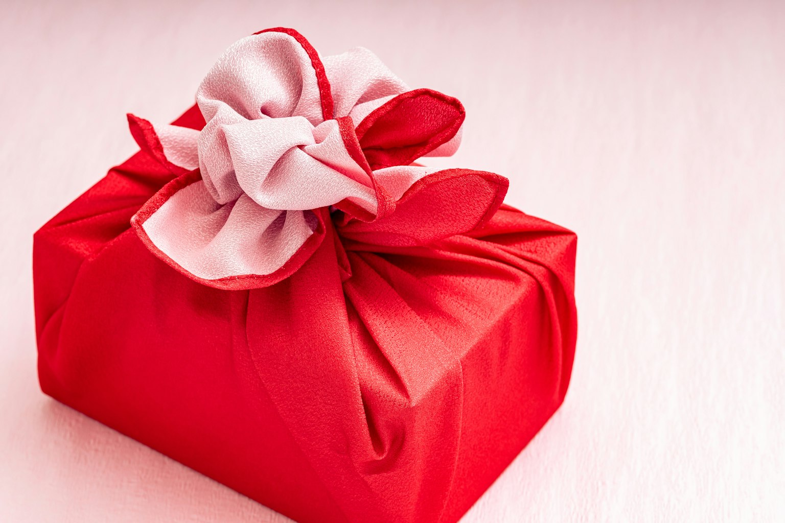 Un cadeau rouge emballé dans un tissu avec un nœud blanc et des pétales décoratifs