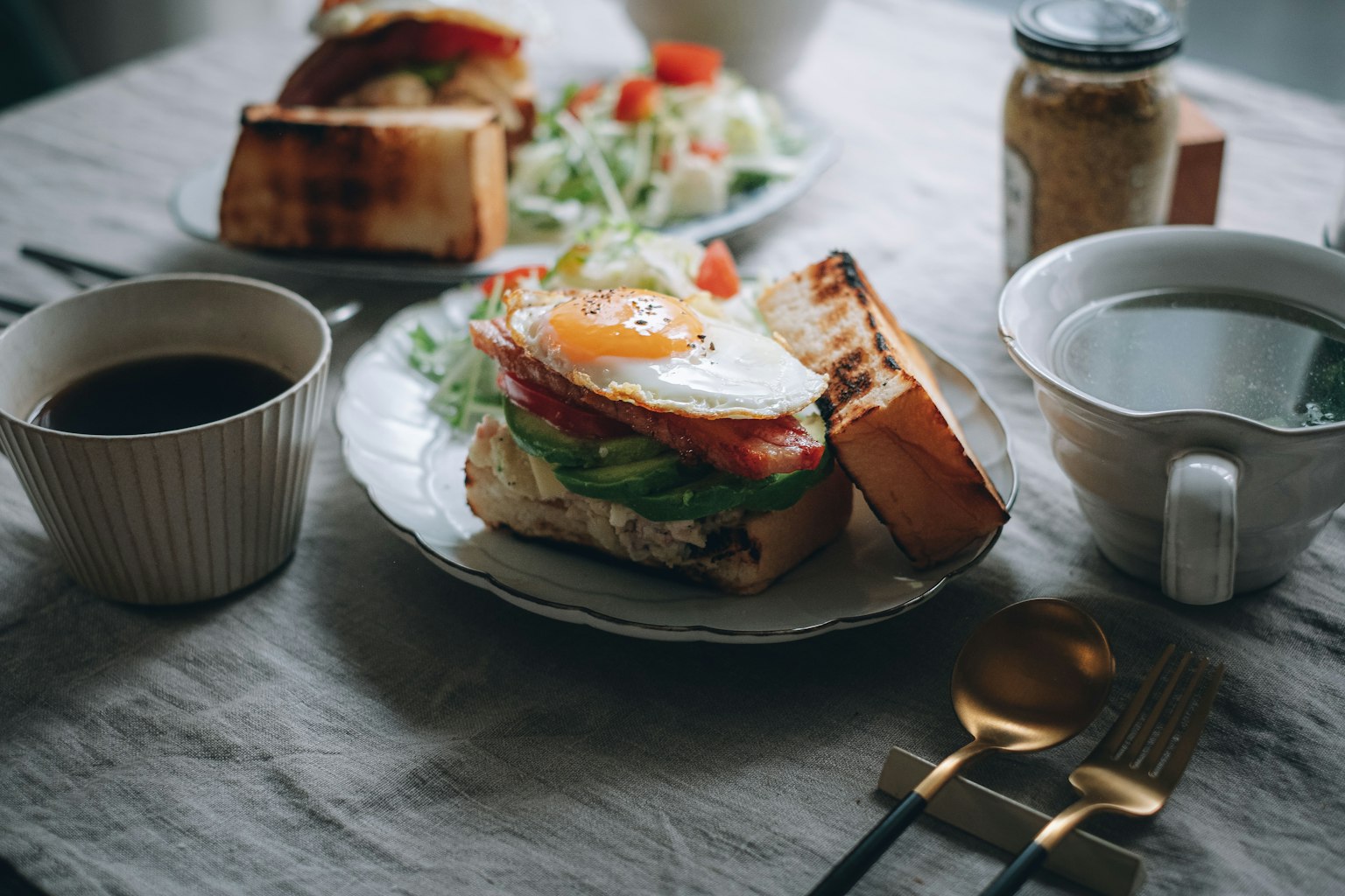 Frühstücksteller mit Sandwich aus Ei und Gemüse Kaffee und Salat auf dem Tisch