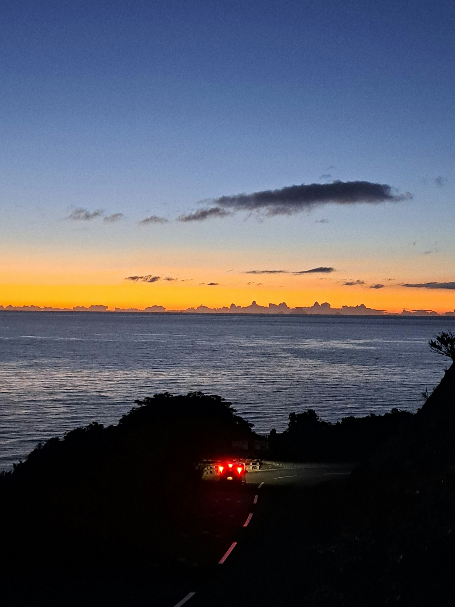日落海岸旁的蜿蜒道路和汽车尾灯