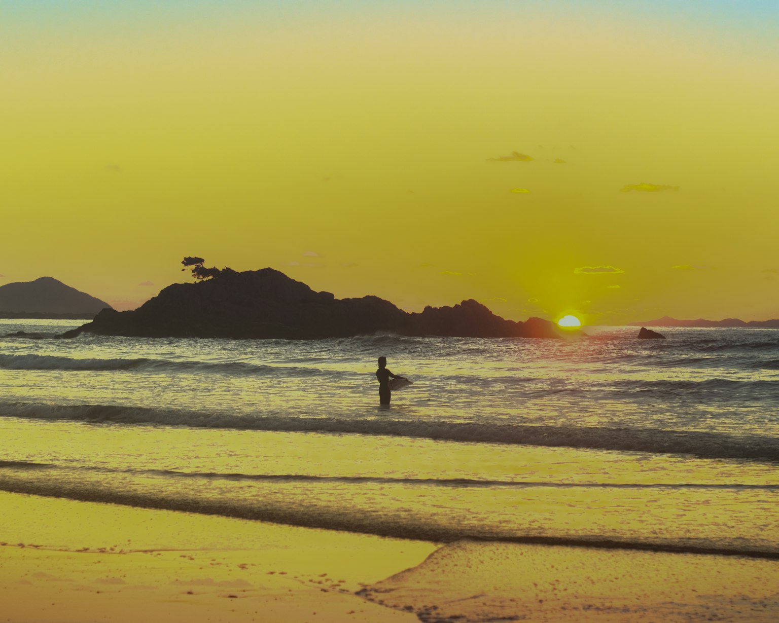 Eine Person, die im Ozean bei Sonnenuntergang mit einer felsigen Insel im Hintergrund watet