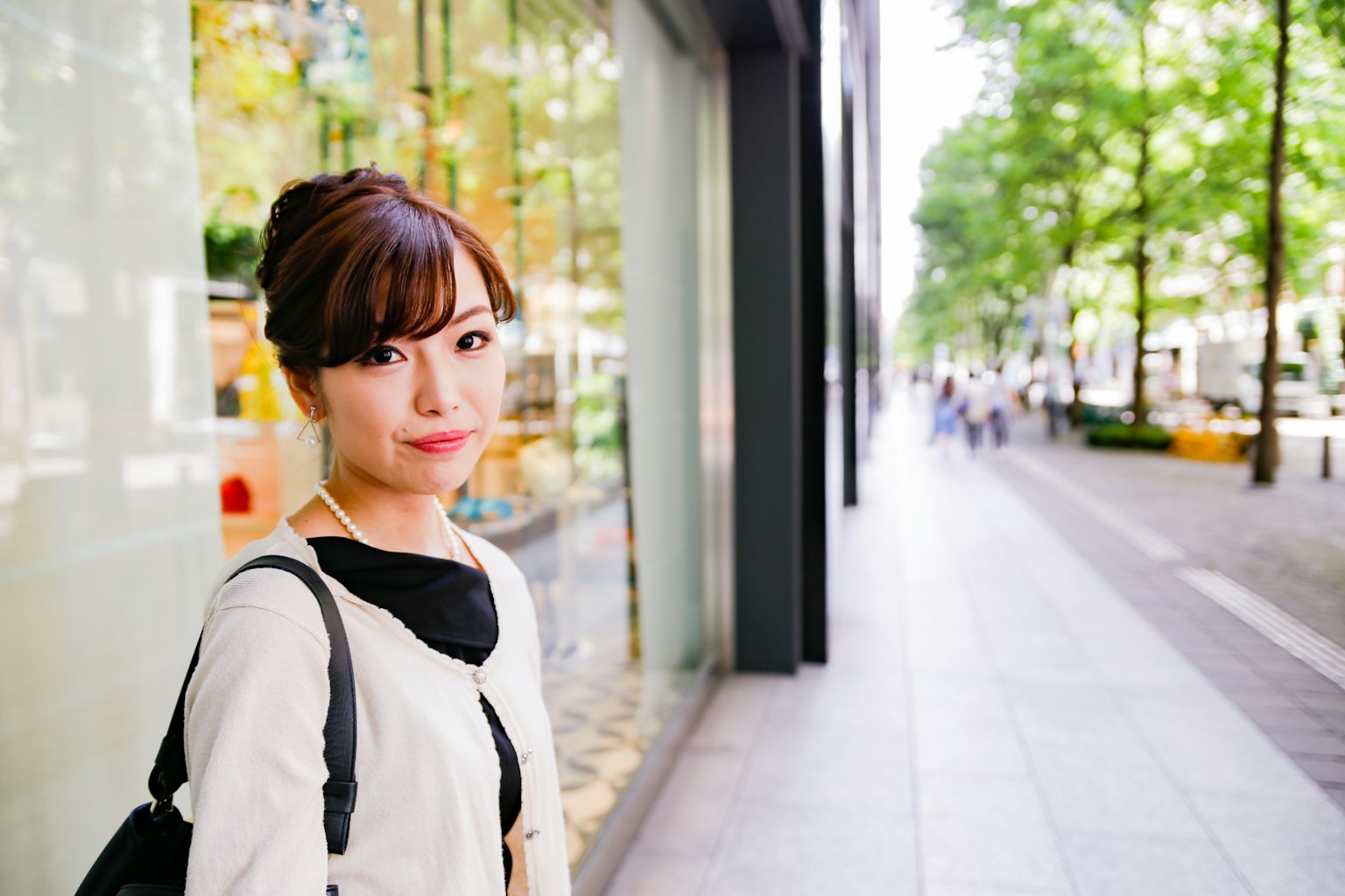 Retrato de una mujer sonriente en una calle de la ciudad con árboles verdes y escaparates al fondo