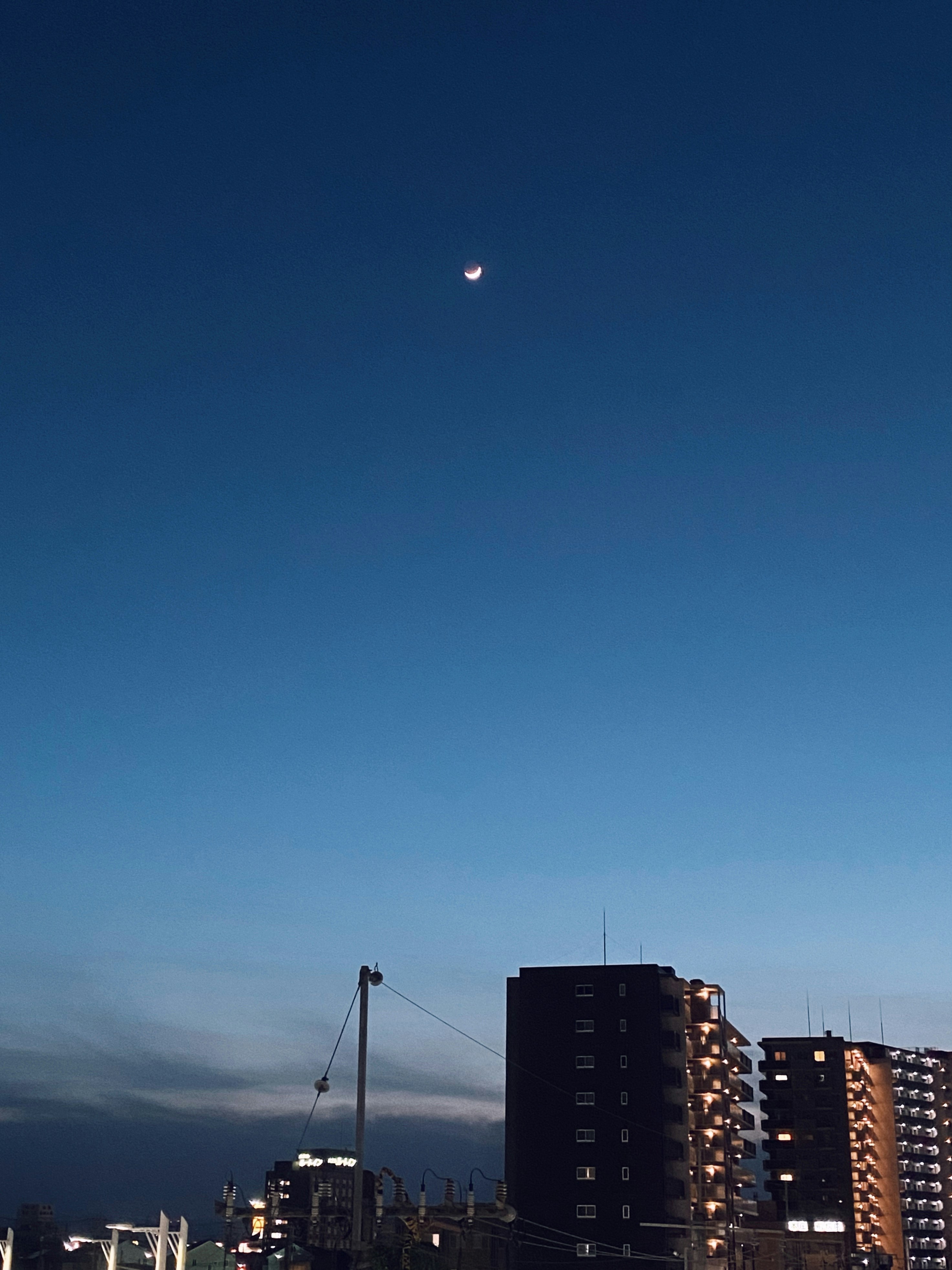 夕暮れの青い空に浮かぶ月と高層住宅のシルエット