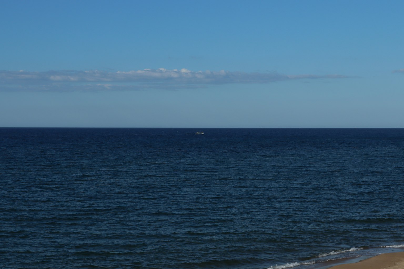 Un vasto mare blu e cielo con una piccola barca visibile in lontananza