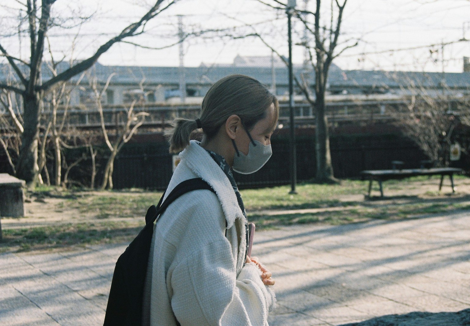 Profil einer Frau mit Maske, die in einem Park mit Bäumen im Hintergrund geht