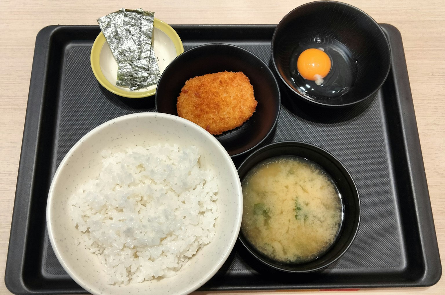 Conjunto de comida japonesa en una bandeja con arroz, sopa miso, huevo, croqueta y un elemento envuelto en papel de aluminio