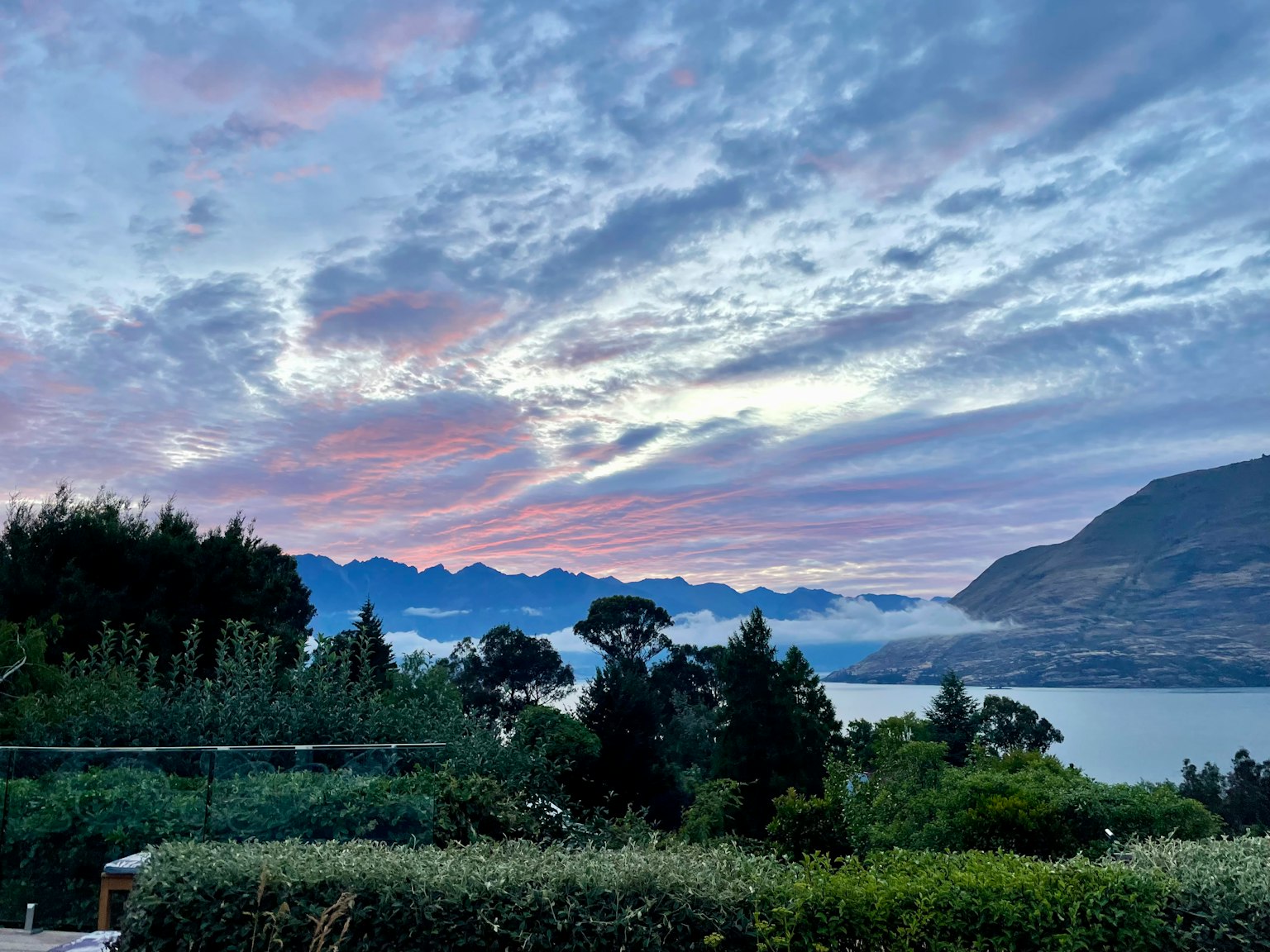 Schöner Sonnenuntergangshimmel über einem See mit blauen Bergen und üppigem Grün