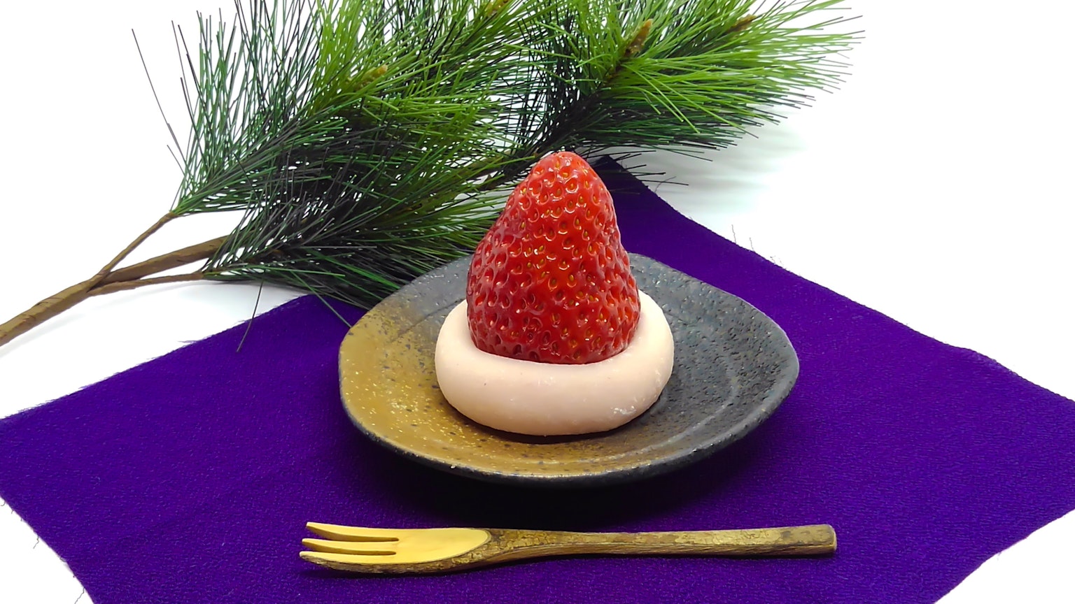 Bánh ngọt Nhật Bản có dâu tây trên bánh mochi trắng đặt trên đĩa tối màu với nĩa vàng và cây thông xanh