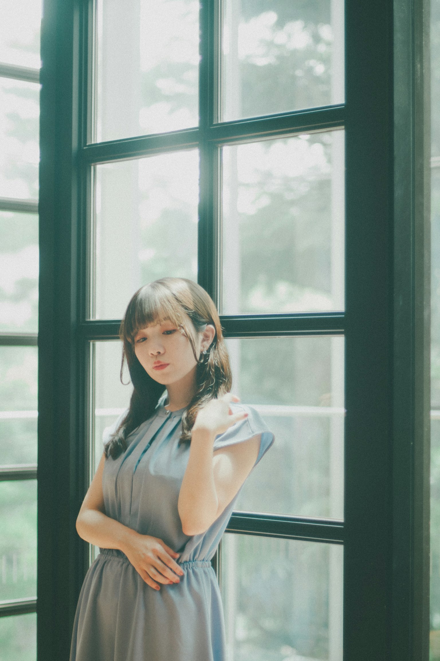 Portrait of a woman standing in front of bright windows wearing a soft blue dress with sunlight streaming in