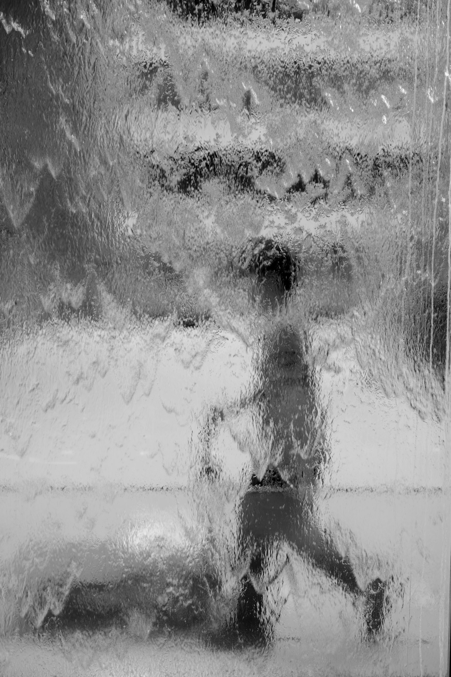 水滴のついたガラス越しに見える子供のシルエットと背景のぼやけた階段