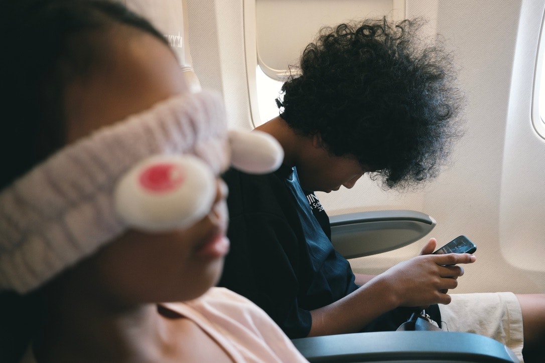 飛行機の機内で子どもと大人がそれぞれスマホを見ている様子