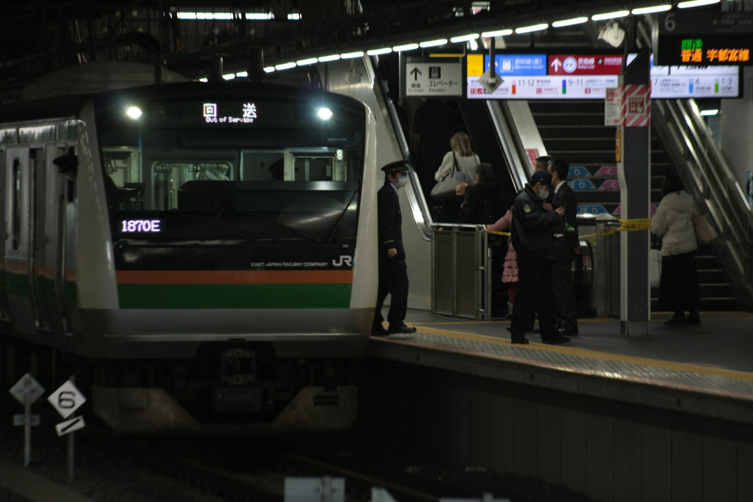 Kereta berhenti di stasiun di malam hari dengan penumpang dan papan petunjuk