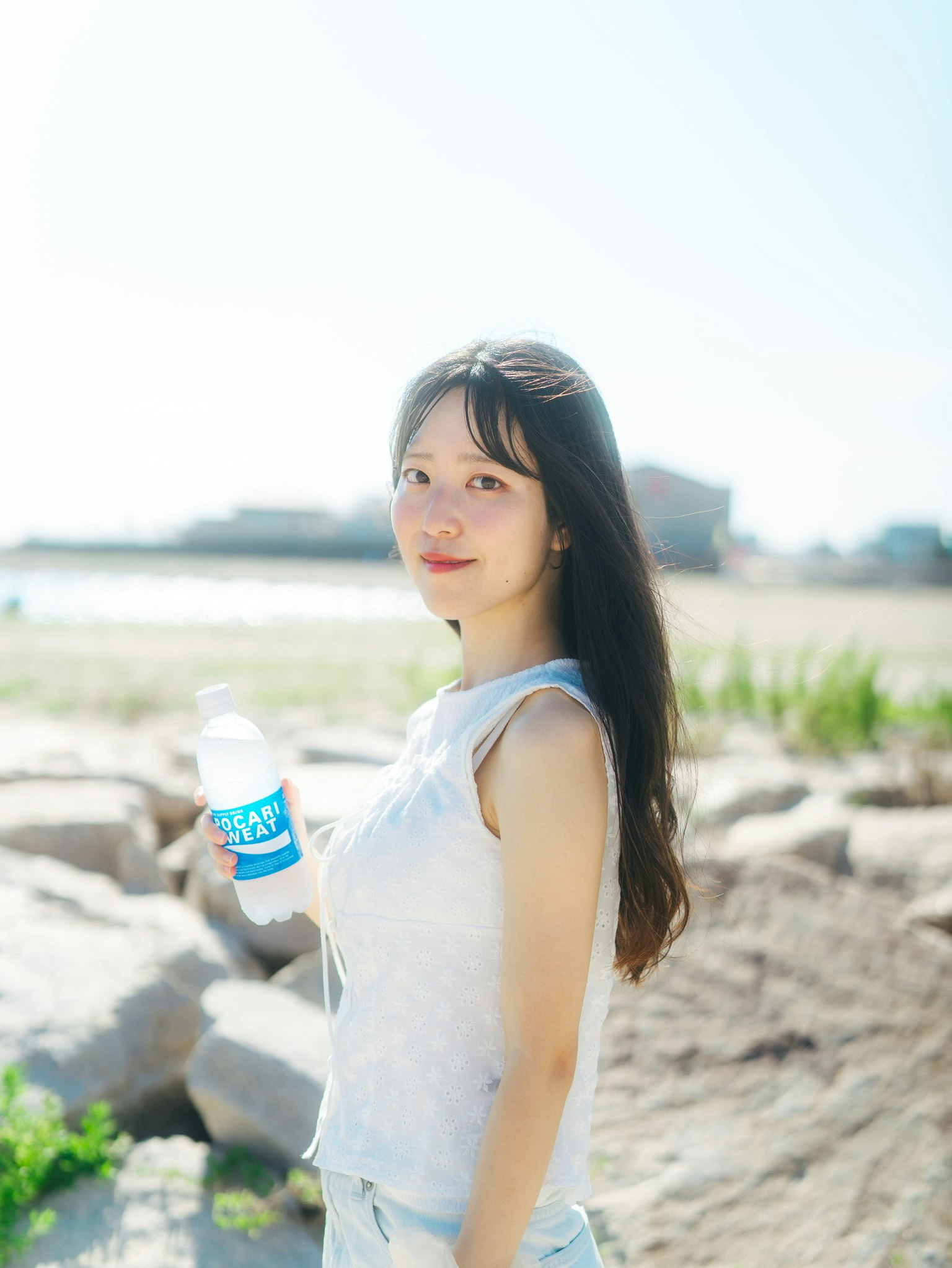 海辺の岩場で青い飲料と赤いリップが映える女性
