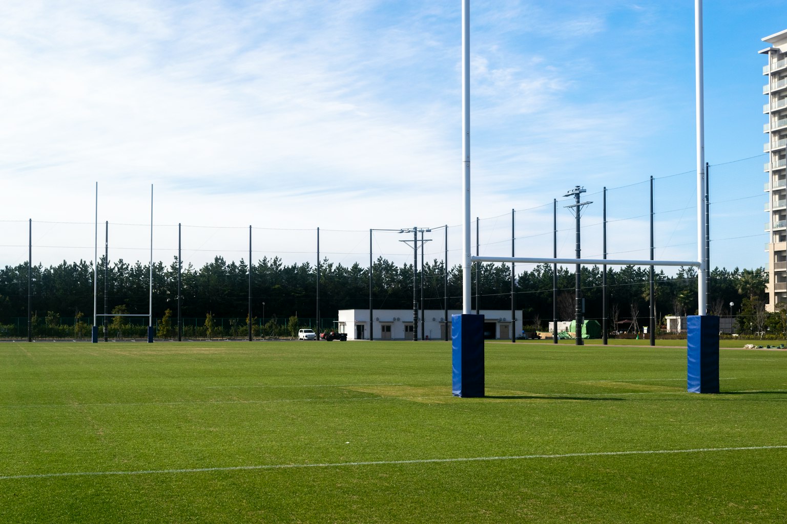 Lapangan rugby dengan tiang gawang biru dan latar belakang pohon serta bangunan