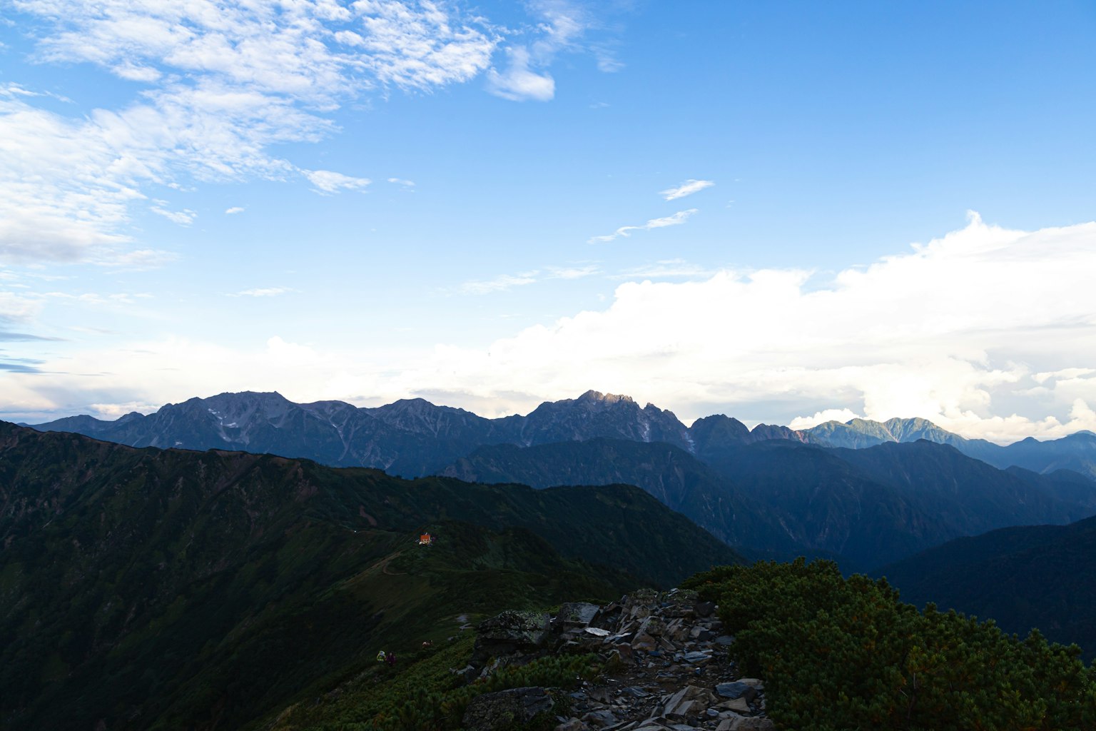 蓝天之下的山脉广阔景观，绿意盎然的山坡和远处的山峰