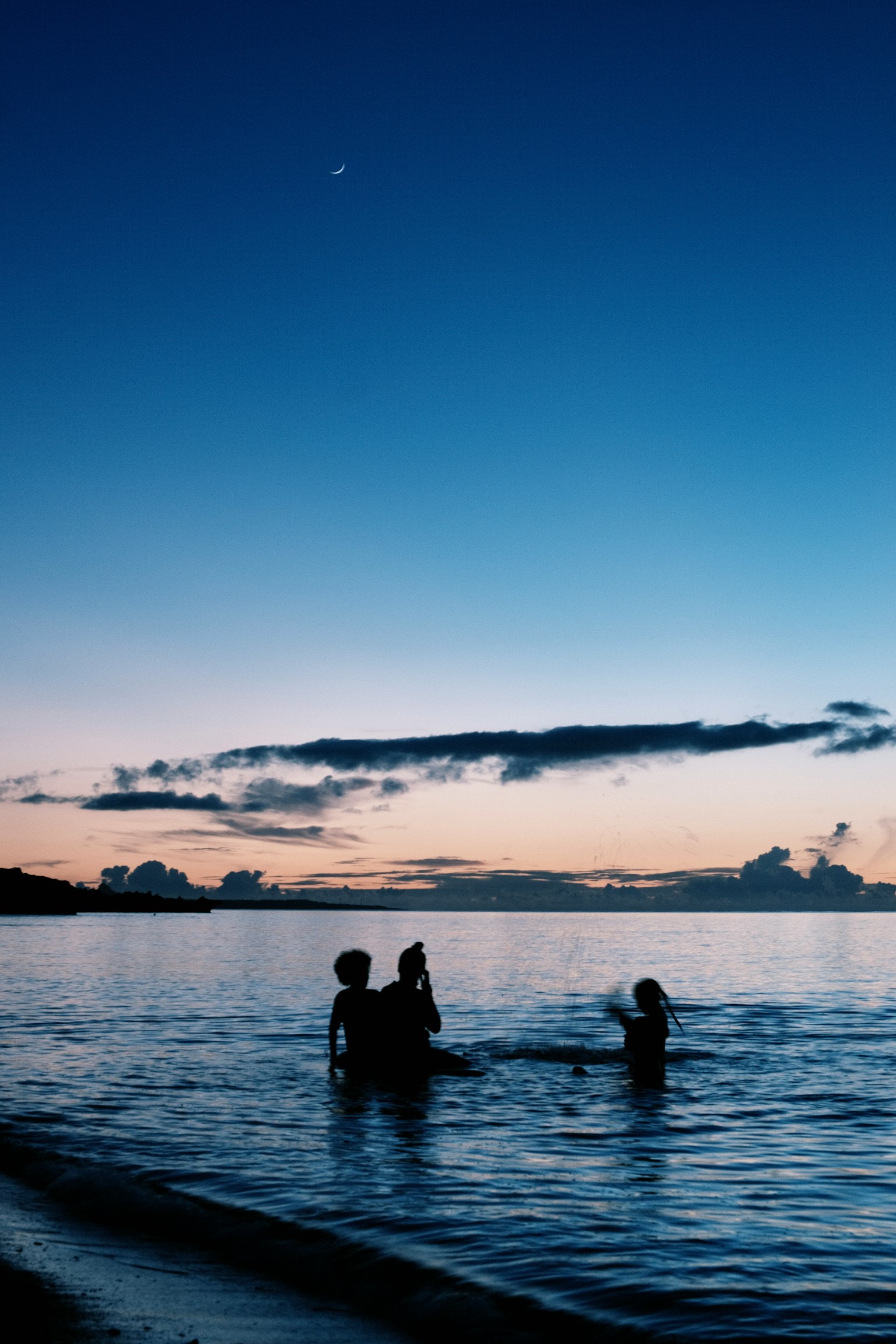 Silhouettes de personnes jouant dans la mer au crépuscule avec un ciel bleu