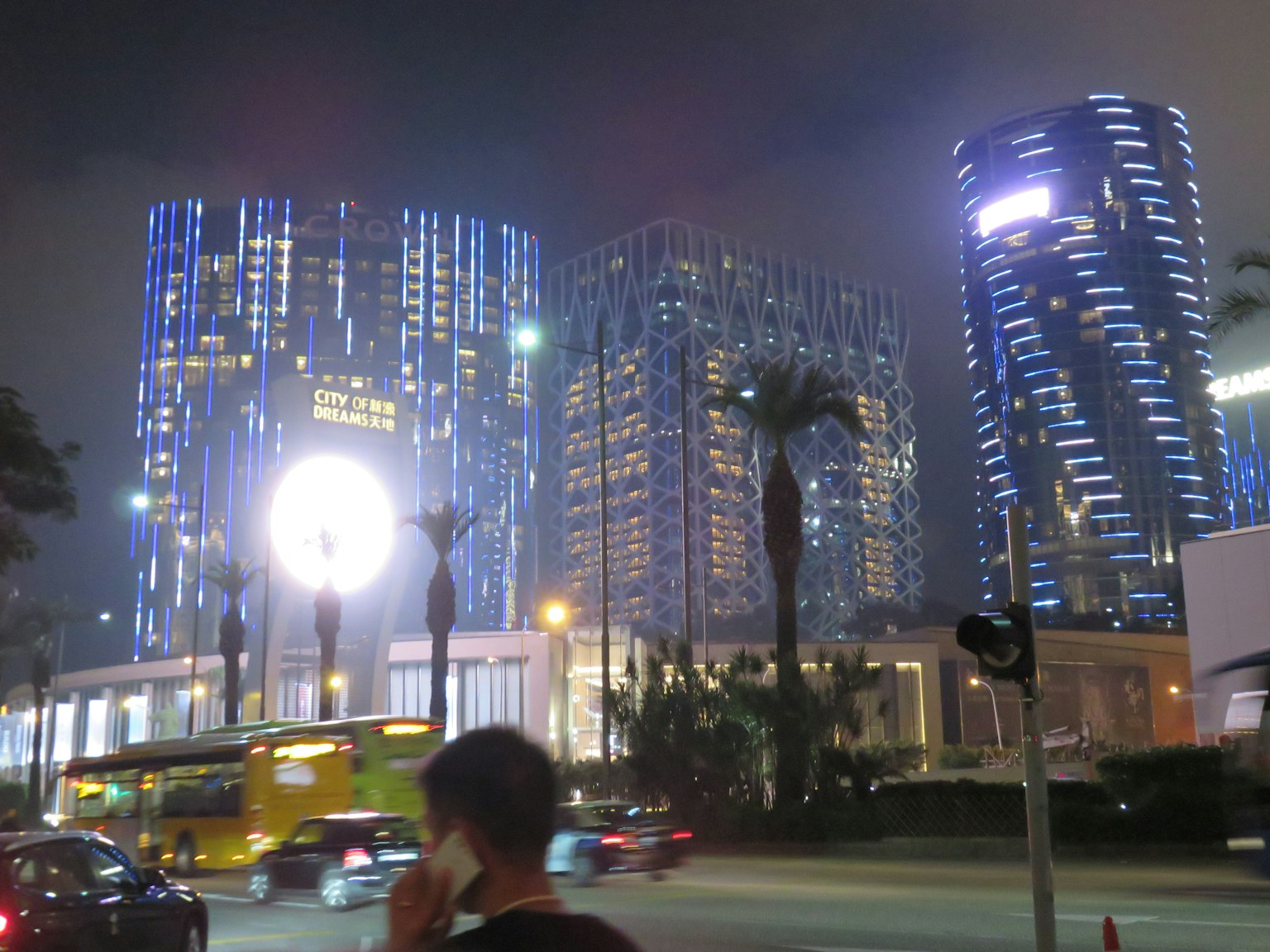 ทิวทัศน์เมืองยามค่ำคืน อาคารสูงสว่างไสวด้วยแสงสีฟ้ามีรถและคนเดินถนน