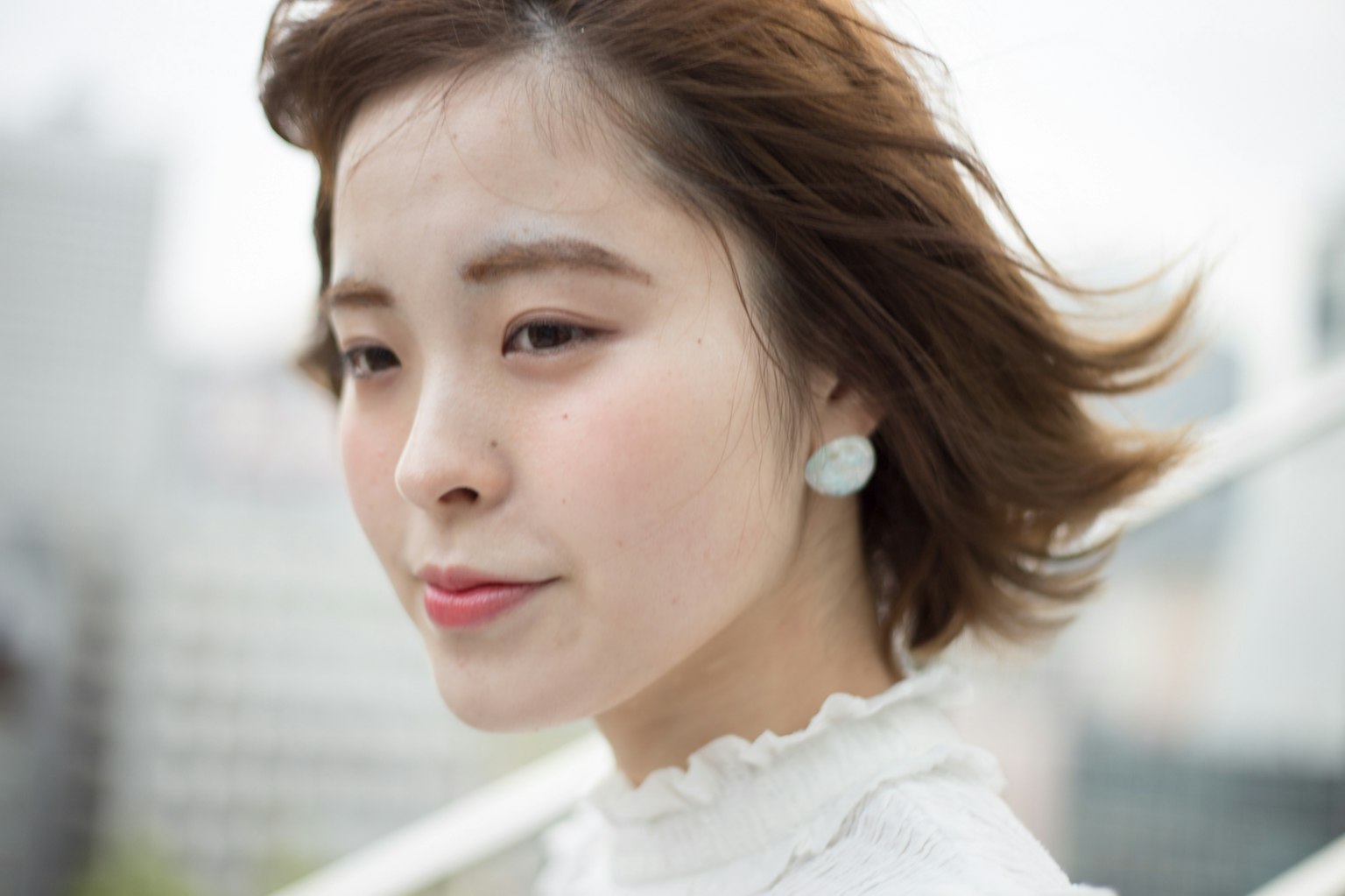 Side profile of a woman with flowing hair wearing a white blouse urban background