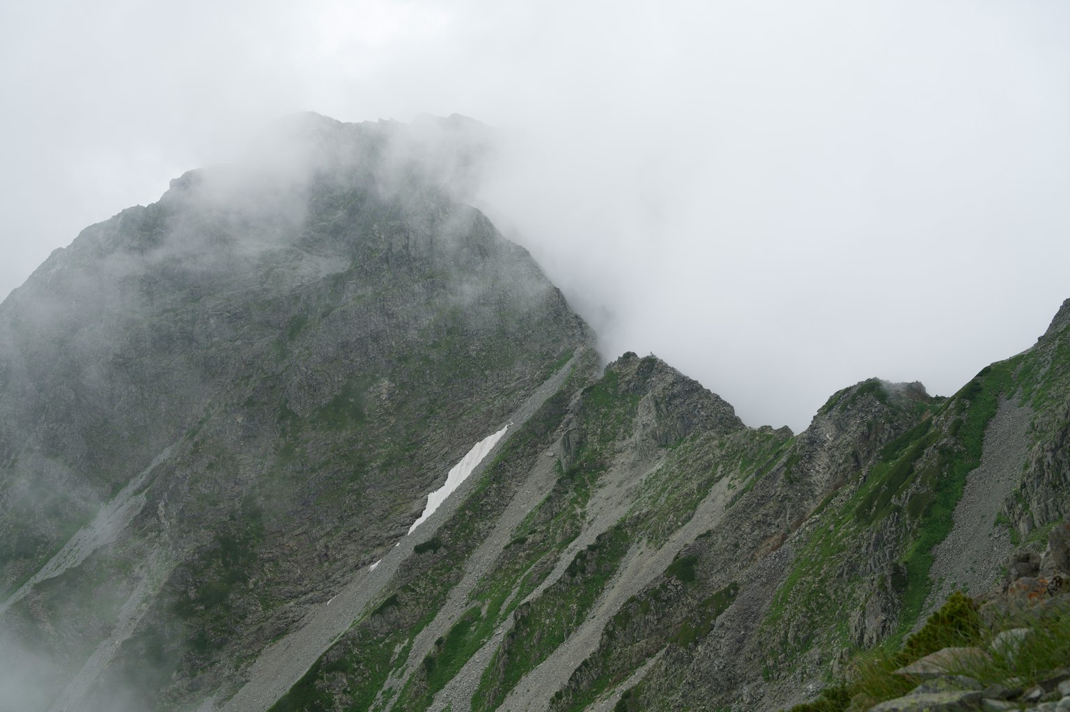Berglandschaft im Nebel mit scharfen Felsgipfeln und grünen Hängen