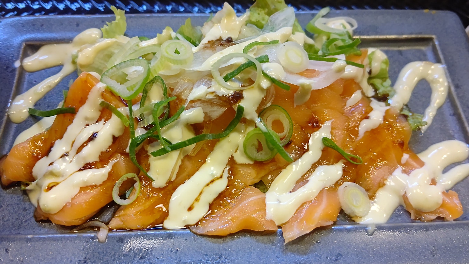Sliced salmon sashimi topped with green onions and mayonnaise