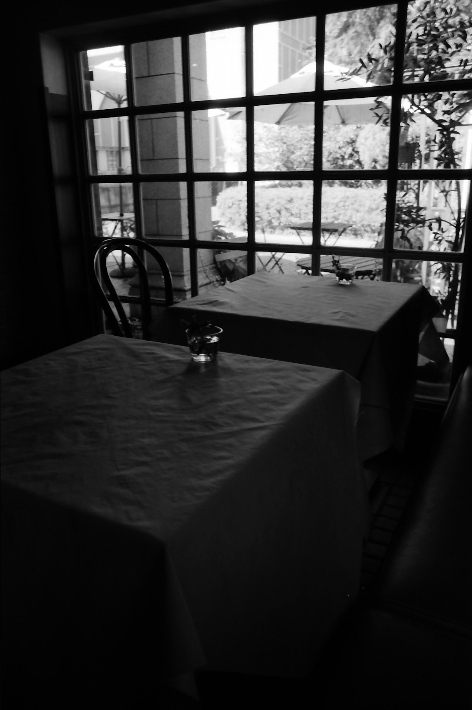 Interior of a restaurant in black and white featuring two tables with white tablecloths and a view of greenery outside the window
