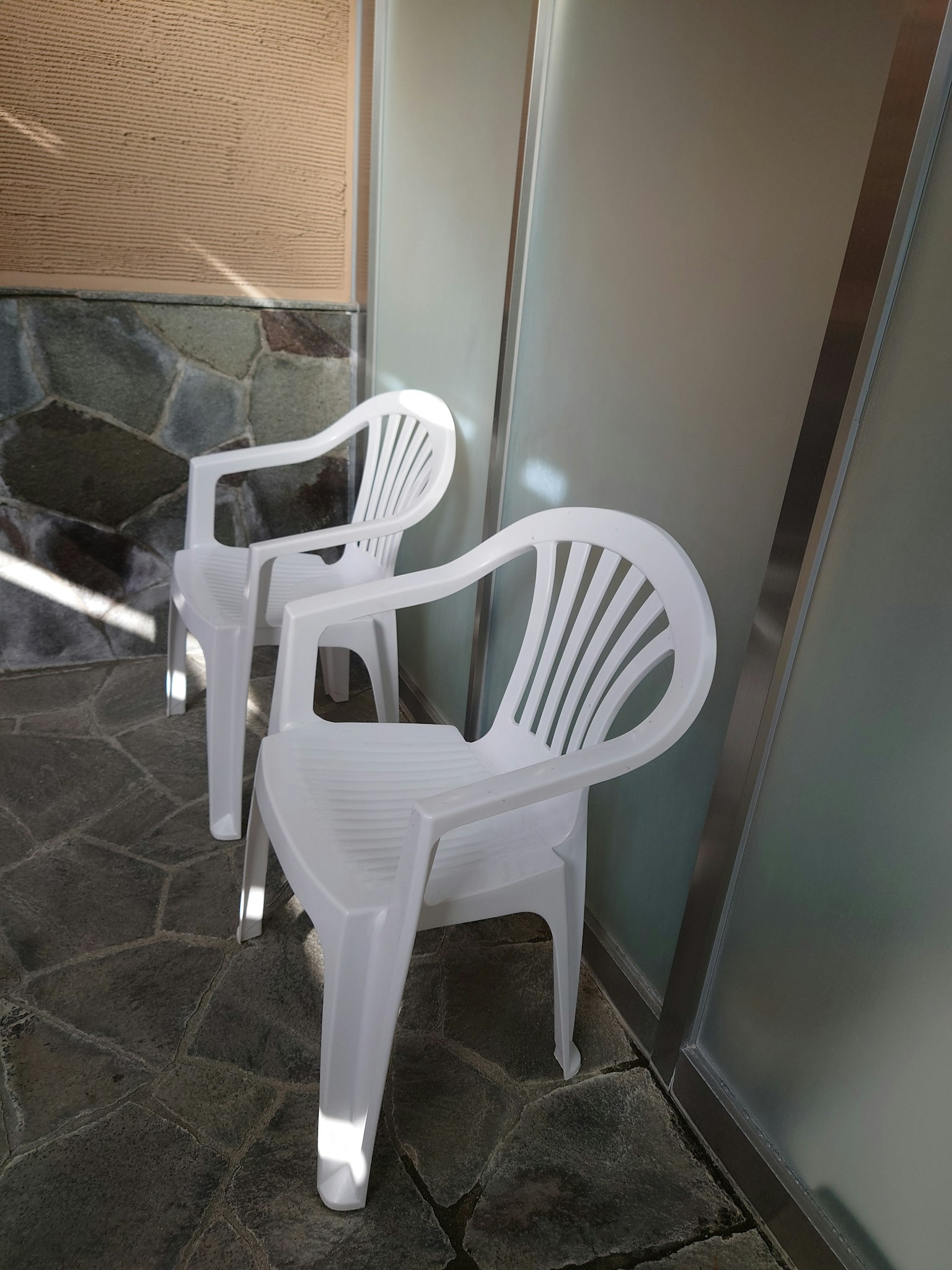Zwei weiße Plastikstühle neben einer Glaswand