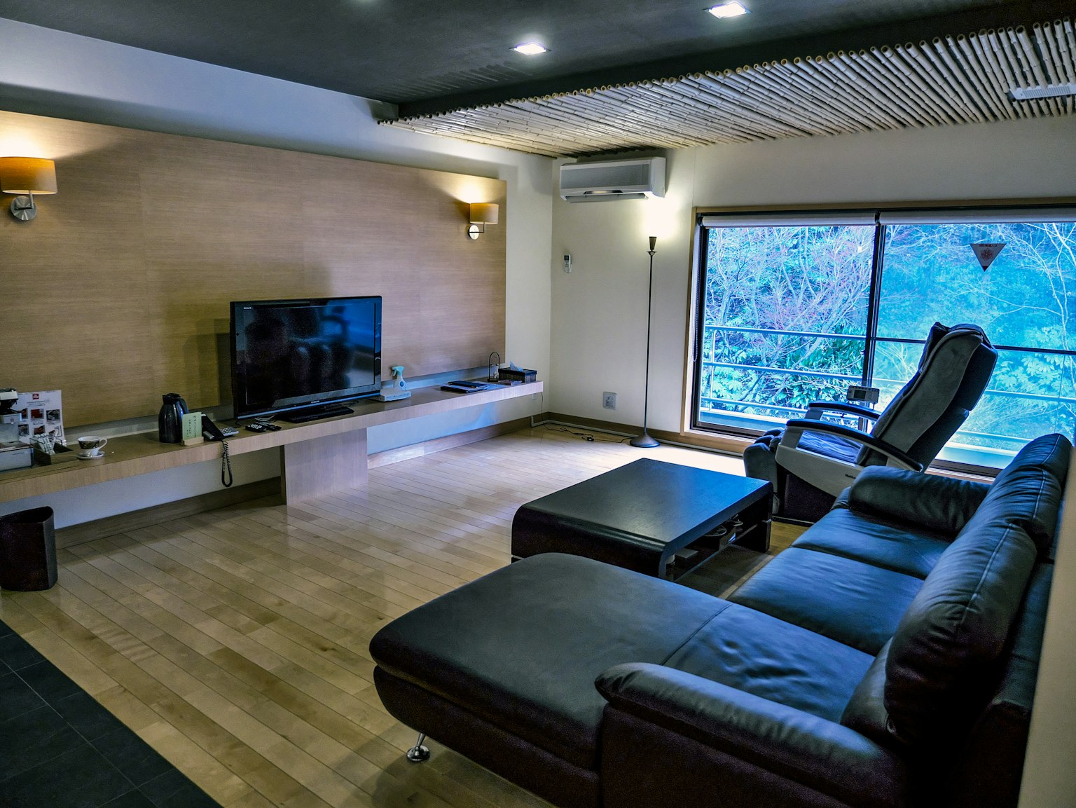 Interior de sala moderna con sofá negro, televisor, luz natural de la ventana