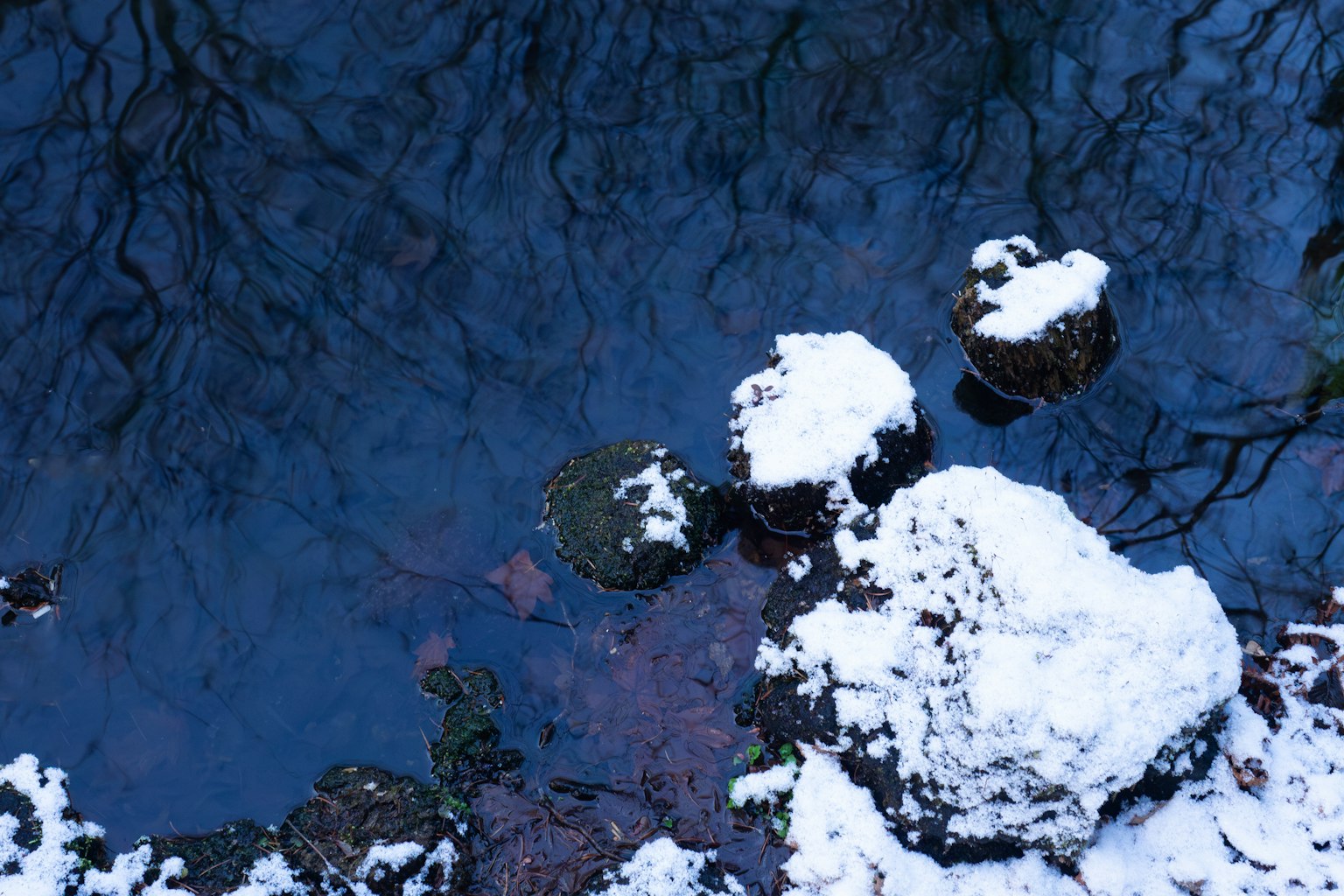Una vista serena di un ruscello con rocce coperte di neve e una superficie d'acqua blu profonda